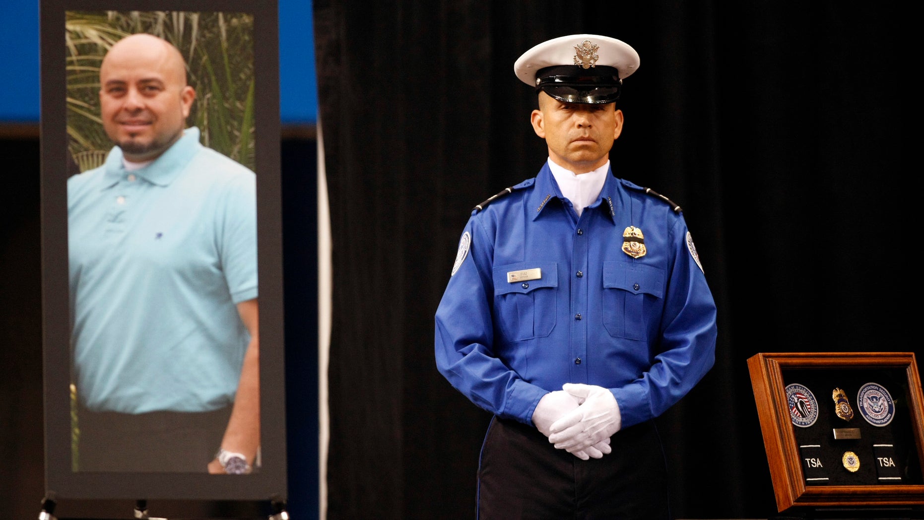 A TSA officer standS in front of a portrait of slain TSA officer Gerardo Hernandez during his public memorial at the Los Angeles Sports Arena, Tuesday, Nov. 12, 2013.
