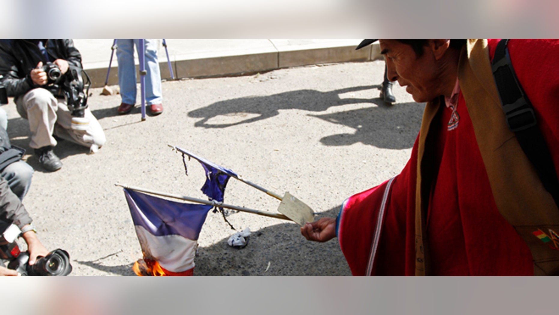 An Aymara indigenous man burns representations of France's national flag outside the French embassy during a protest over France's alleged refusal to let the Bolivian president's plane cross over French airspace, in La Paz, Bolivia, Wednesday, July 3, 2013. Bolivia's Foreign Minister David Choquehuanca says the plane bringing President Evo Morales home from Russia was rerouted to Austria after France and Portugal refused to let it to cross their airspace because of suspicions that NSA leaker Edward Snowden was on board. (AP Photo/Juan Karita)