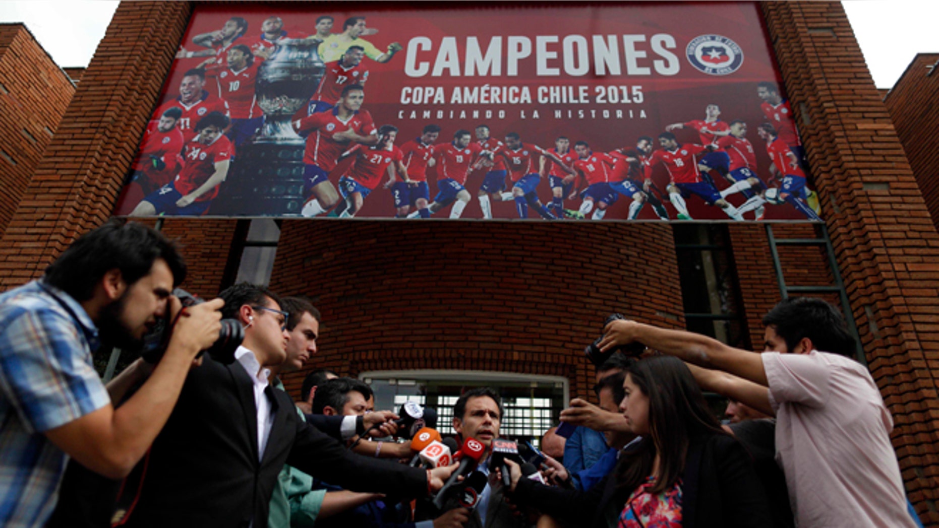 Government Attorney Carlos Gajardo, center, speaks to the press, in front of Chile's National Association of Professional Soccer, ANFP, after police investigators entered the building to look for documents and computers from the office of former president of the ANFP, Sergio Jadue, in Santiago, Chile, Thursday, Dec. 3, 2015. U.S. prosecutors confirmed that Jadue had pleaded guilty to charges of racketeering conspiracy and wire fraud conspiracy, in relation to the recent FIFA scandal. As part of their plea, Jadue agreed to forfeit all funds on deposit in his U.S. account. (AP Photo/Luis Hidalgo)