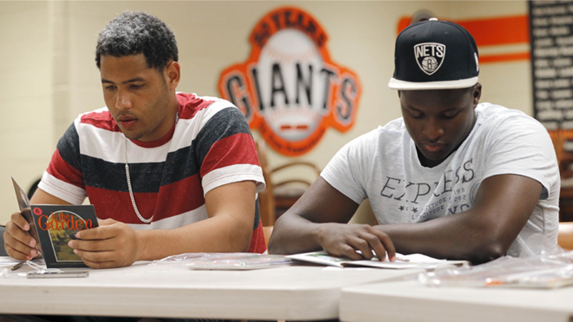 In this May 22, 2014 photo, San Francisco Giants baseball prospects Jose Murel and Sandy Perez, right, read beginner English books in class in Scottsdale, Ariz. San Francisco is just one of many clubs putting a stronger emphasis on teaching English basics, including training as to writing checks, using a bank account or mailing a letter. (AP Photo/Matt York)
