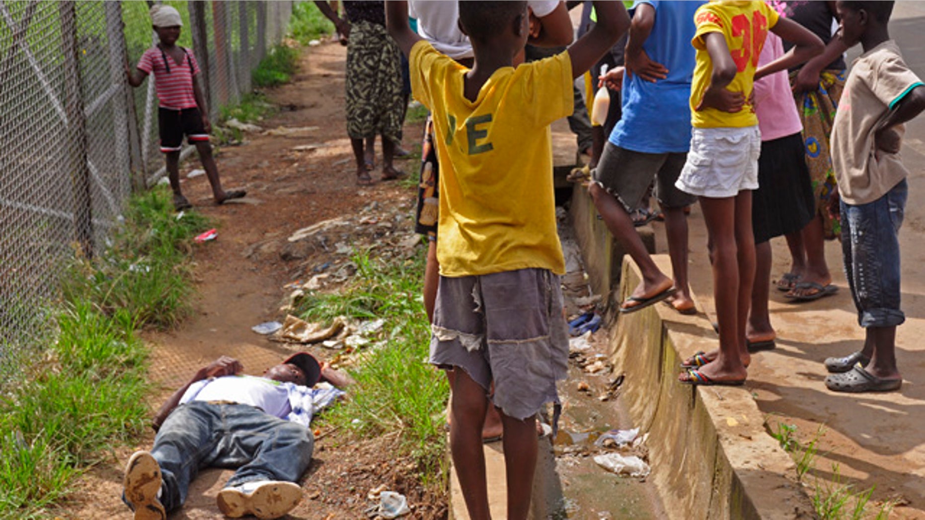 August 19, 2014: Children surround a man, left, who fell down while walking on a street suspected of having contracted the Ebola virus in the city of Monrovia, Liberia. The World Health Organization says the outbreak has killed more than 1,200 people, while authorities struggle to contain its spread and treat the sick. (AP Photo/Abbas Dulleh)