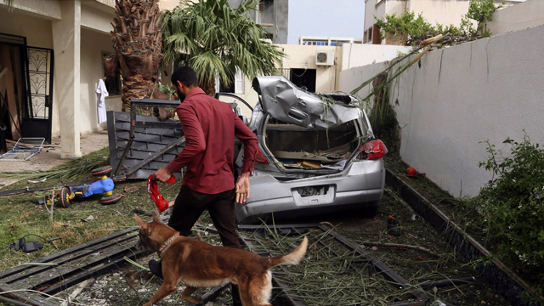 April 23, 2013: A security officer using a sniffer dog inspects the site of a car bomb that targeted the French embassy wounding two French guards and causing extensive material damage in Tripoli, Libya.