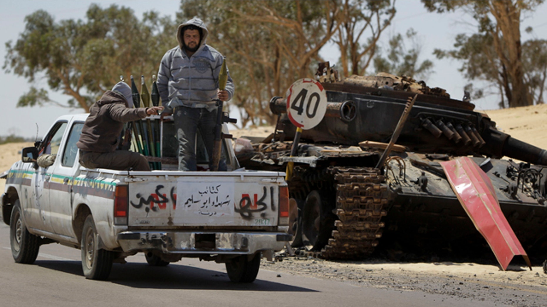 April 10, 2011: Rebel fighters armed with rocket propelled grenade launchers head back into Ajdabiya, past a previously destroyed pro-Gadhafi forces tank, during heavy shelling there, in Libya.