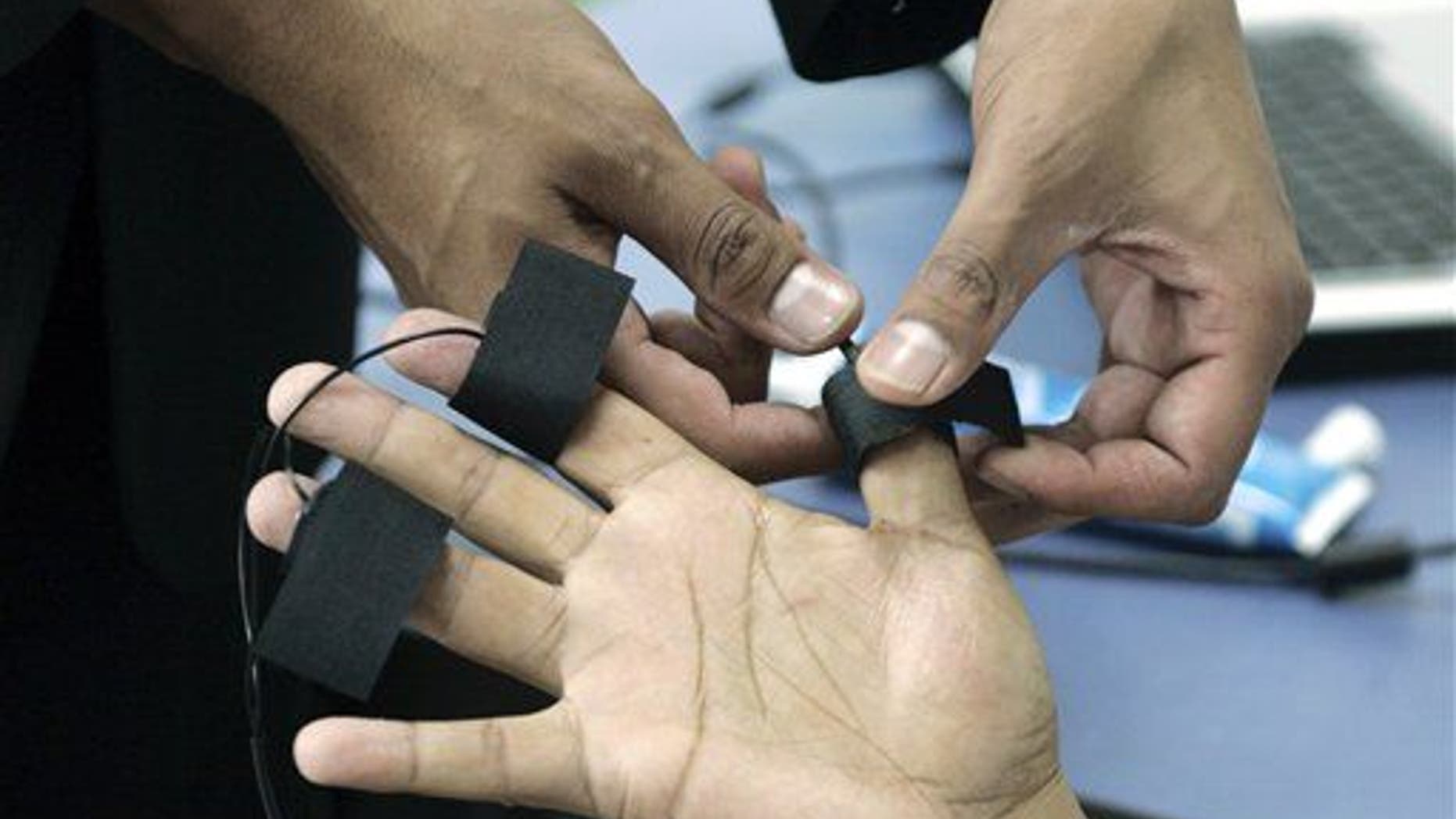 A polygraph examiner applies electrodes on the fingers of a subject.