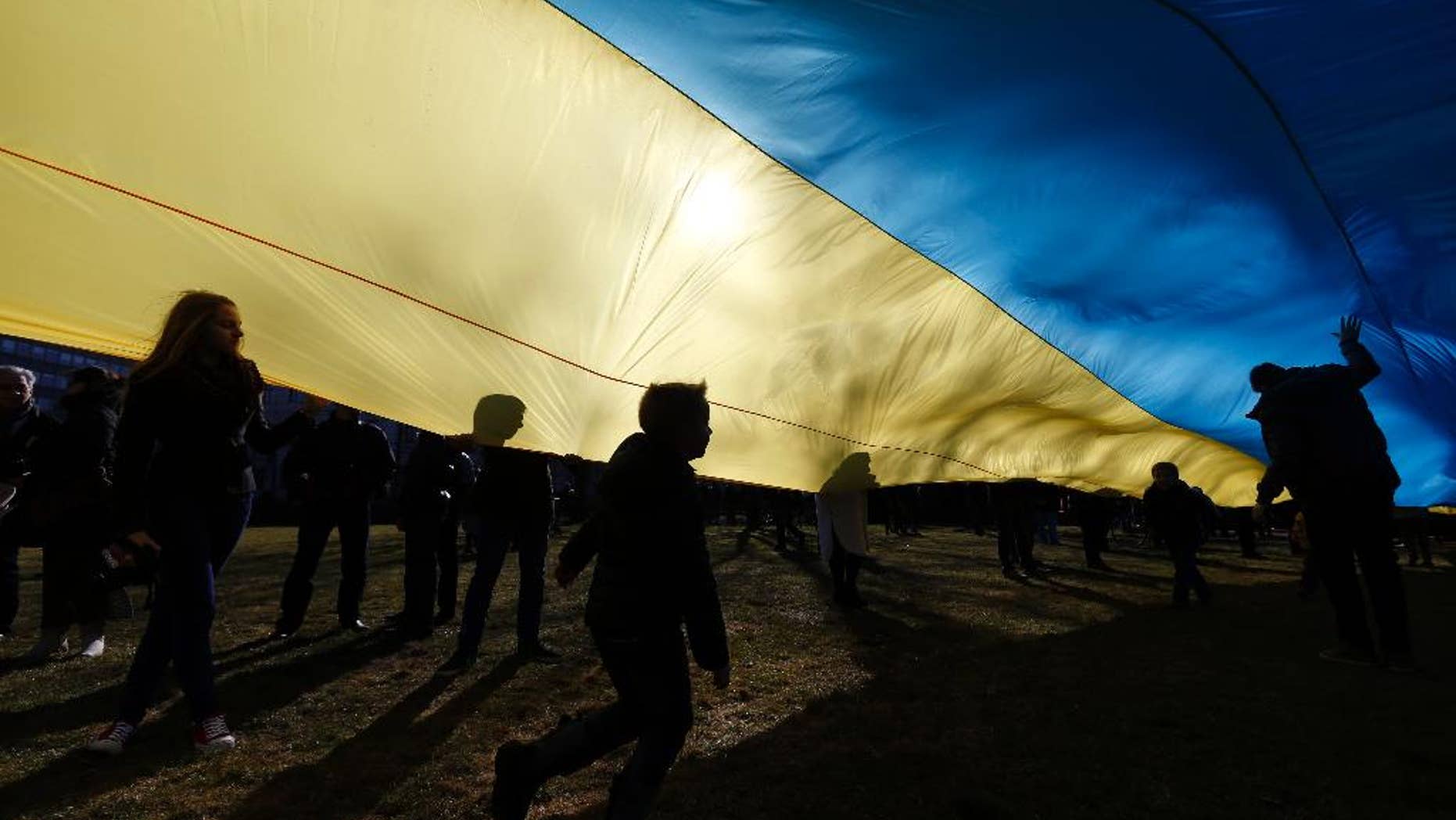 Children play as people hold up a giant Ukrainian flag to protest against the Russian intervention in Ukraine during the celebration of Lithuania's independence in Vilnius, Lithuania, Tuesday March 11, 2014. Lithuania celebrated the anniversary of its declaration of independence from the Soviet Union on Thursday, recalling the seminal events that set the Baltic nation on a path to freedom and helped lead to the collapse of the U.S.S.R. (AP Photo/Mindaugas Kulbis)