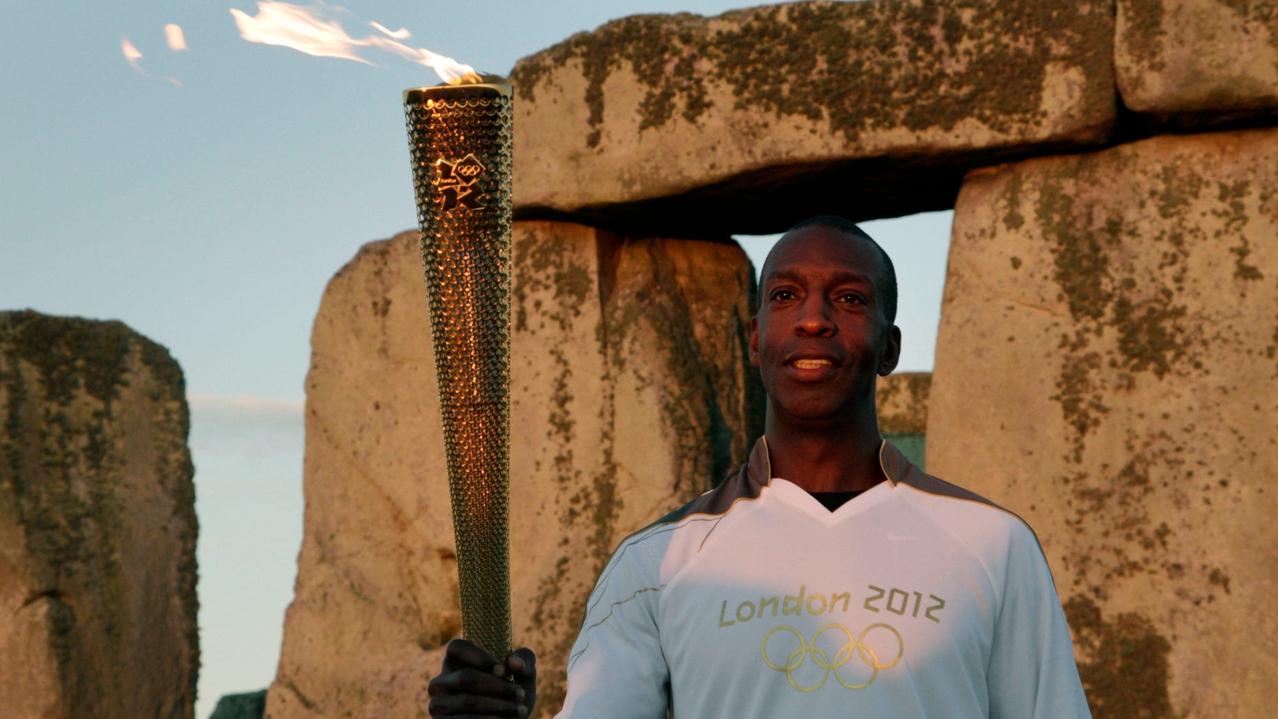 July 12, 2012: U.S. Olympian sprinter Michael Johnson poses for photographers holding the Olympic Flame at Stonehenge, England.