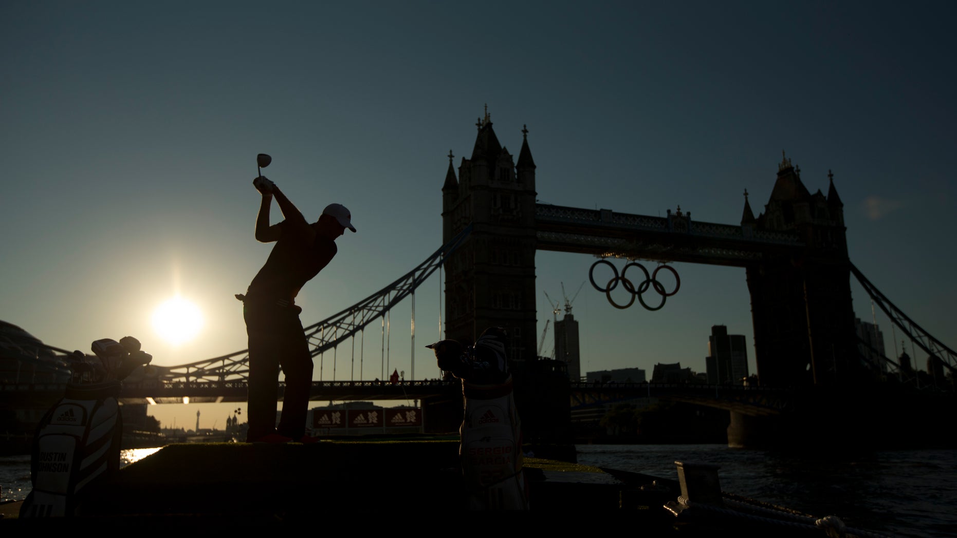 U.S. golfer Dustin Johnson is silhouetted as he takes a swing in a posed picture for photographers as Olympic rings hang from Tower Bridge.