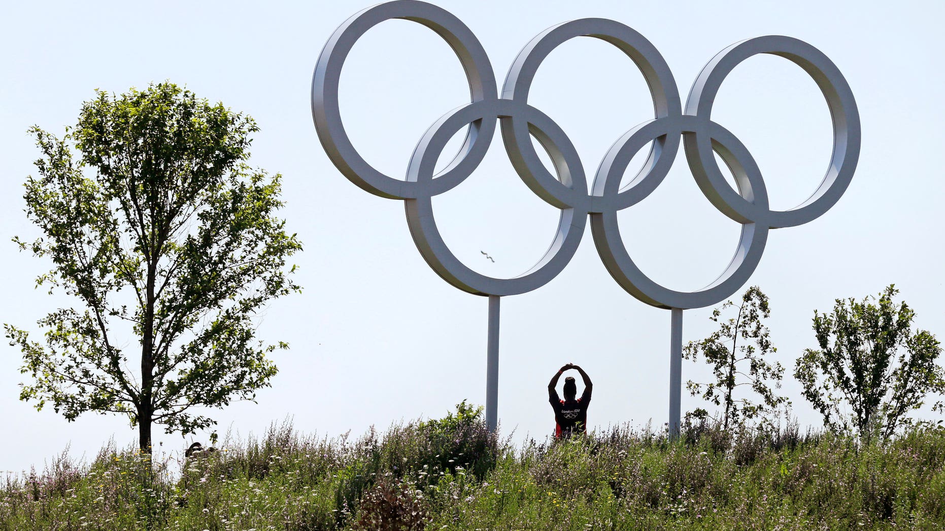 Volunteer Abby Idowu, of London, stretches under the Olympic rings while being photographed by friends on the other side of a hill at Olympic Park prior to the 2012 Summer Olympics, Thursday, July 26, 2012, in London. The opening ceremonies for the games will be held Friday, July 27. (AP Photo/Charles Krupa)