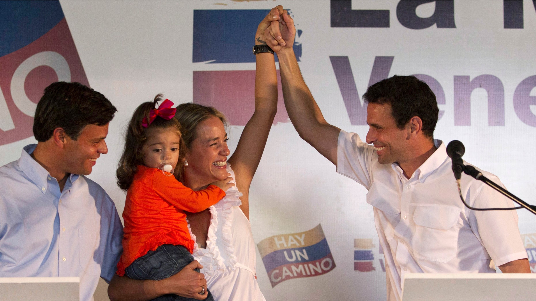 Opposition politician Leopoldo Lopez, puts his arm around the waist of his wife Lilian Tintori as she holds their daughter Manuela, 2, and raises her left hand with presidential candidate Henrique Capriles Radonski at a news conference in Caracas, Venezuela, Tuesday Jan 24, 2012. (AP Photo/Ariana Cubillos))