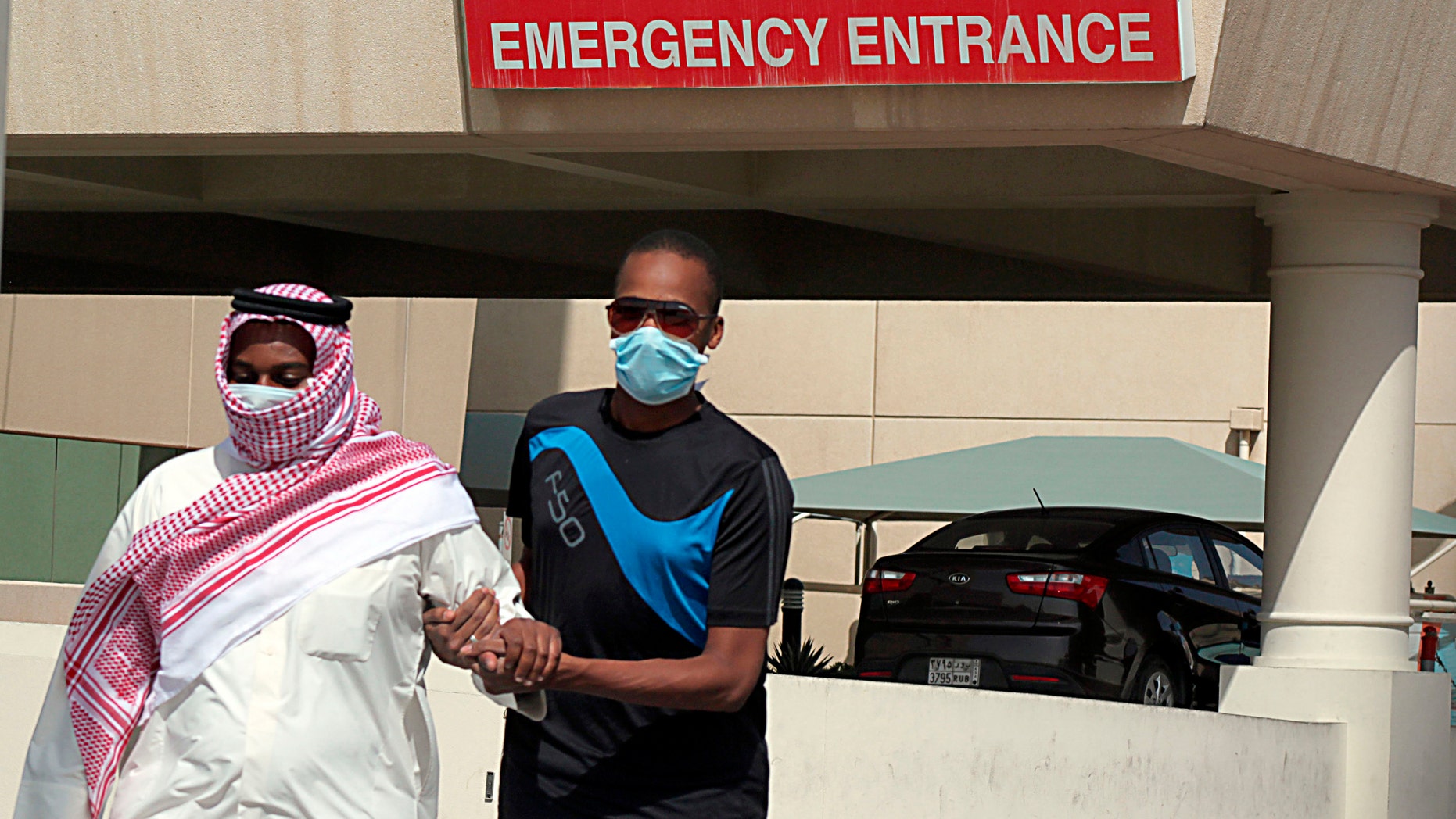 A man, wearing a surgical mask as a precautionary measure against the novel coronavirus, helps a friend who has the common flu near a hospital in Khobar city in Dammam May 23, 2013.