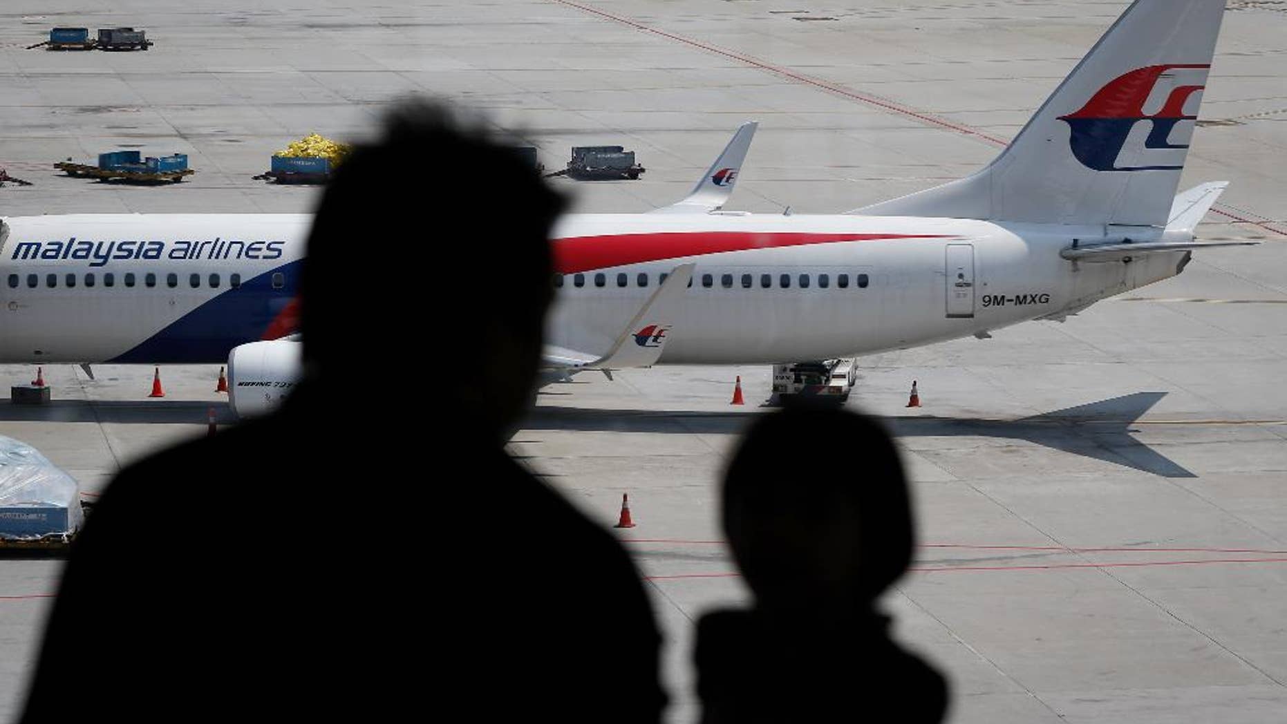 In this Friday, Feb. 27, 2015 photos, visitors look out from a viewing gallery as a Malaysia Airlines plane sits in the tarmac at the Kuala Lumpur International Airport (KLIA) in Sepang, Malaysia. After a year of unprecedented calamity for the Southeast Asian carrier, Malaysia Airlines is aiming to return to profitability by 2017 with a drastic $1.7 billion overhaul that includes cutting nearly a third of its staff. (AP Photo/Vincent Thian)