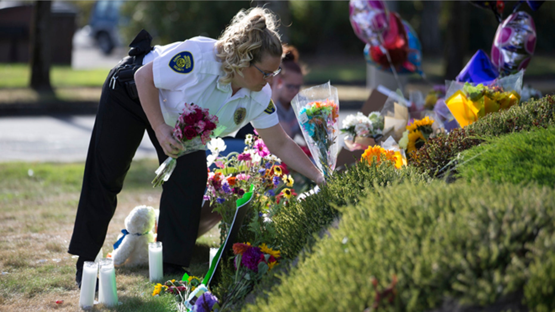 A security guard working at the Cascade Mall places flowers at a makeshift memorial on Sunday, Sept. 25, 2016, in Burlington, Wash., to the five victims killed in a shooting at the mall on Friday. The 20-year-old man suspected of killing the five people with a rifle at a Macy's makeup counter had a string of run-ins with the law in recent years, including charges he assaulted his stepfather. (AP Photo/Stephen Brashear)