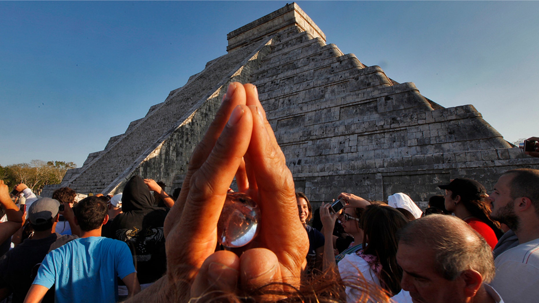 A man holds a crystal above his head as he and over 15,000 people congregate in front of the famous pyramid at Chichen-Itza, Mexico to celebrate the arrival of the Equinox signaling the beginning of Spring, Sunday, March 20, 2011. The famous Mayan ruin is popular at the Equinox when the serpent's back shows on the side of the stairway that leads to the top. (AP Photo/Standard Times , Peter Pereira)