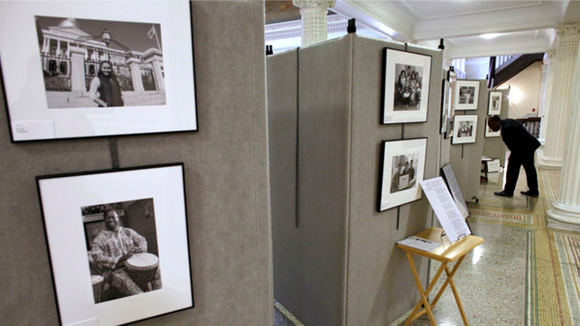 In this Thursday, Nov. 17, 2016 photo Teddy Chery, of Medford, Mass., right, pauses to examine an image that forms part of an exhibit by photographer Mark Chester at the Statehouse, in Boston. Cape Cod-based Chester has produced a collection of photographs of immigrants from all over the world called The Bay State: A Multicultural Landscape - Photographs of New Americans. (AP Photo/Steven Senne)
