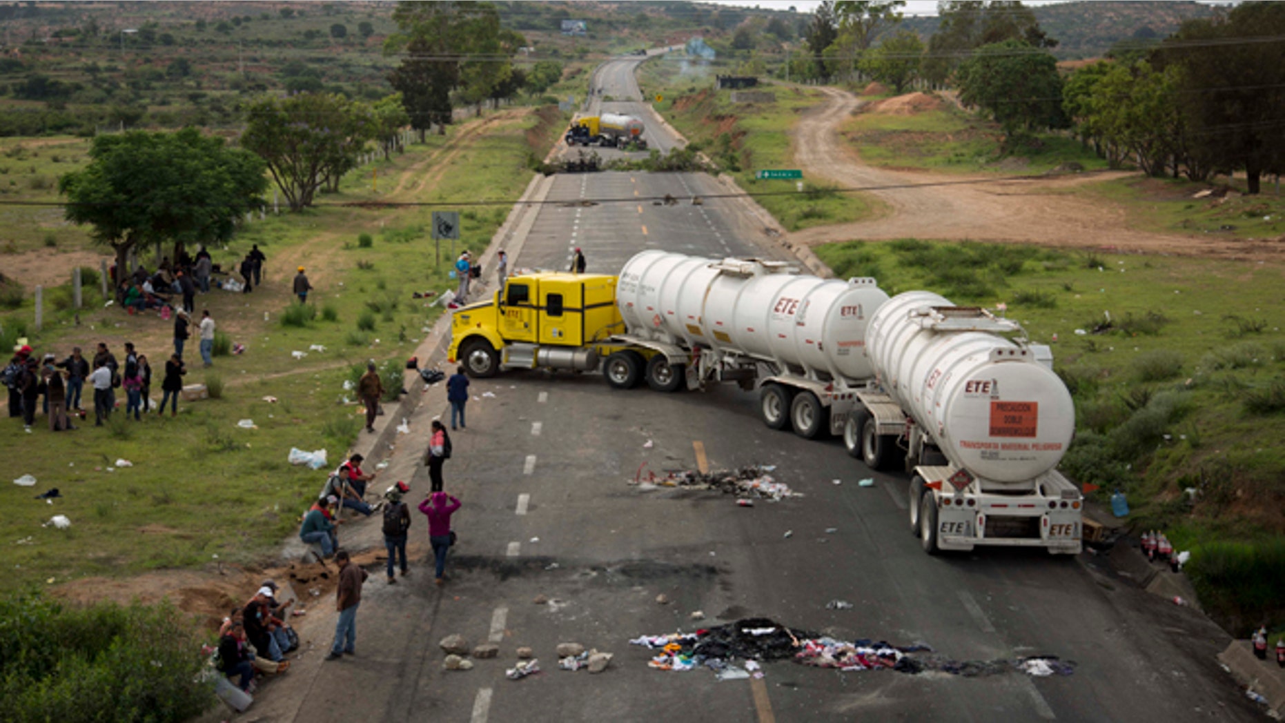 Protesters stand beside trucks blocking the highway in the state of Oaxaca, near the town of Nochixtlan, Mexico, Monday, June 20, 2016. Mexican police say few teachers were involved in violence at a weekend highway protest in the southern state of Oaxaca in which six people died. The teachers are protesting against plans to overhaul the country's education system which include federally mandated teacher evaluations. (AP Photo/Eduardo Verdugo)