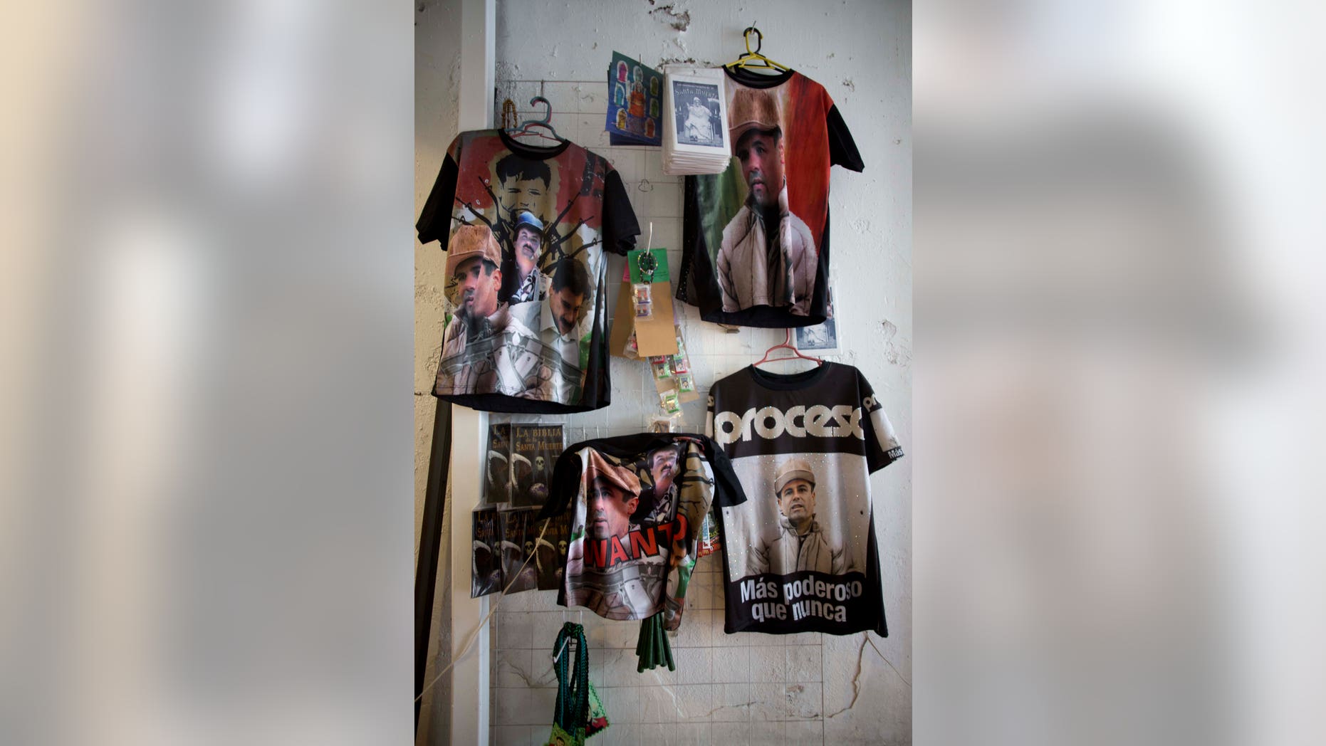 T-shirts featuring fugitive Mexican drug lord Joaquín "El Chapo" Guzmán hang for sale inside the shrine of a faith healer in Mexico City, Friday, Oct. 16, 2015. The government is offering a reward of 60 million pesos, or about $3.5 million dollars, for Guzmán's recapture after he made his second escape from a maximum security prison through an underground tunnel in 2015. (AP Photo/Eduardo Verdugo)