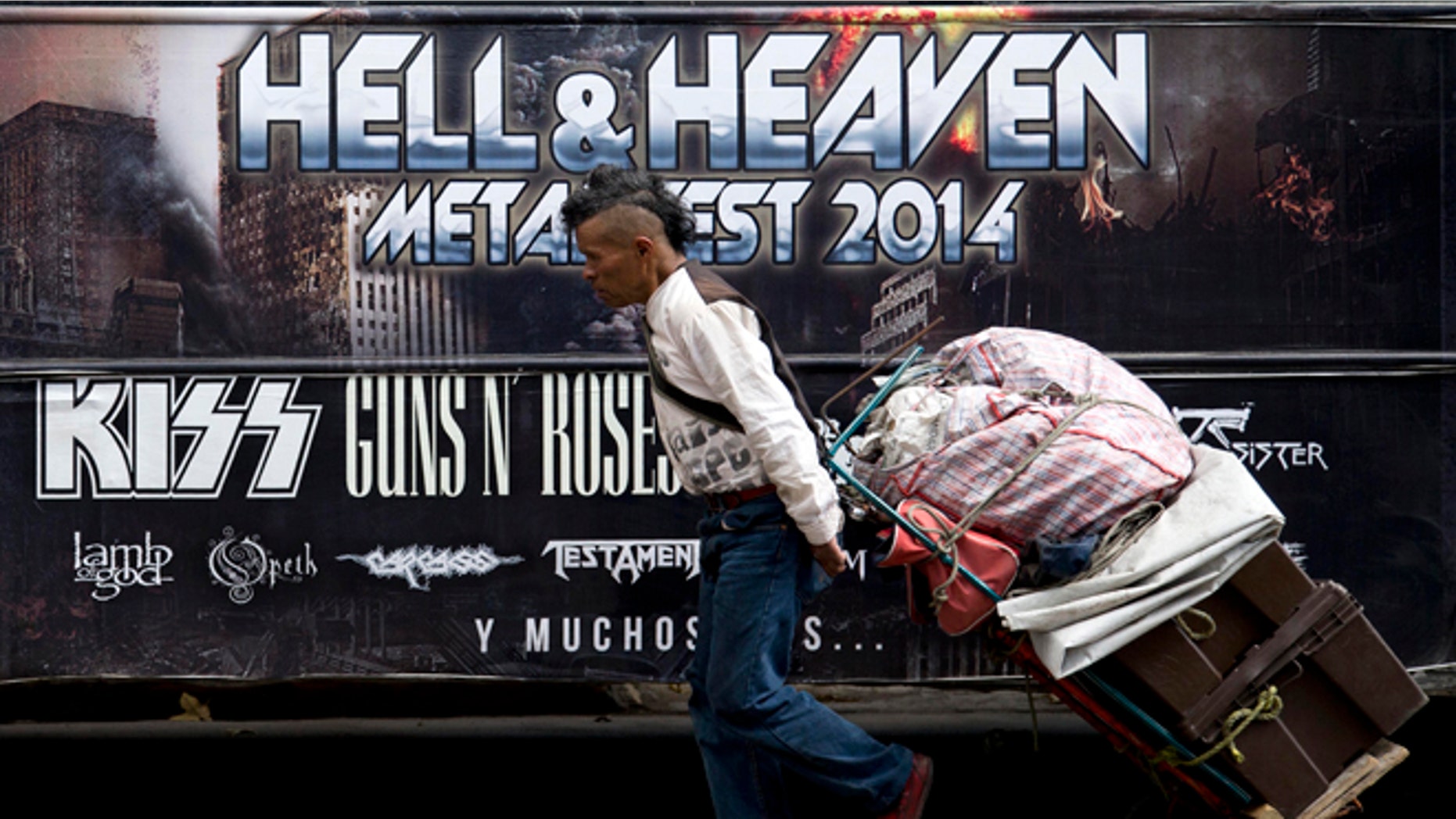 A man pulls a dolly loaded with supplies past publicity of "Hell and Heaven Metal Fest" concert, posted on bus in Mexico City, Friday March 7, 2014. The Mexico state government canceled the concert saying the March 15-16 "Hell and Heaven Metal Fest" planned for a fairground just east of Mexico City did not have adequate safety plans, posing a risk to concert-goers. (AP Photo/Eduardo Verdugo)
