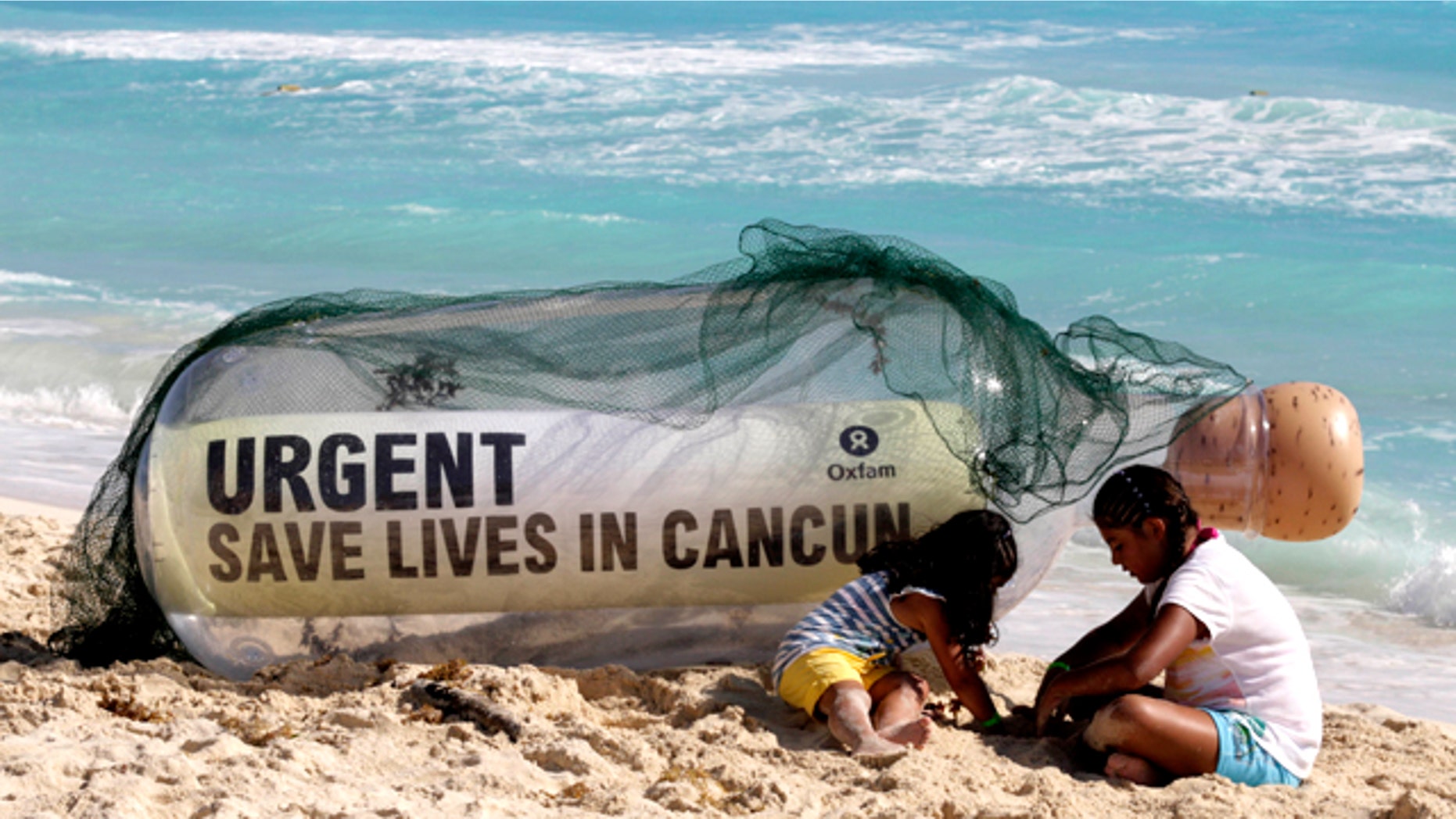 A giant message in a bottle from Oxfam International sits on the beach next to children playing in Cancun, Mexico, Sunday, Nov. 28, 2010. Facing another year without a global deal to curb climate change, the world's nations will spend the next two weeks in Cancun, Mexico, during the annual conference of the 193-nation U.N. climate treaty, debating how to mobilize money to to tackle a changing climate.