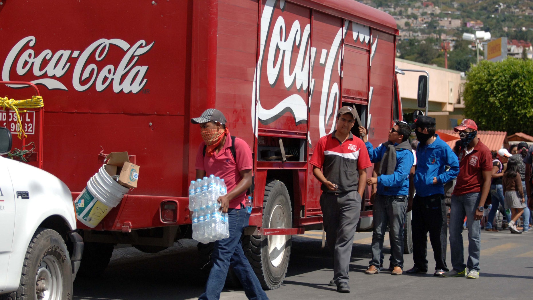 In this Nov. 4, 2014 photo, masked protesters begin to empty a Coca-Cola distribution truck in the city of Chilpancingo, Mexico. Coca-Cola Femsa SA, the brand's largest bottler in Mexico, has temporarily suspended operations in the capital of the embattled state of Guerrero following attacks on its workers and its trucks. The decision comes amid protests in the southern state around the disappearance of 43 students. Protesting students and teachers have regularly blockaded roads and taken over vehicles delivering everything from milk to snacks. (AP Photo/Alejandrino Gonzalez)