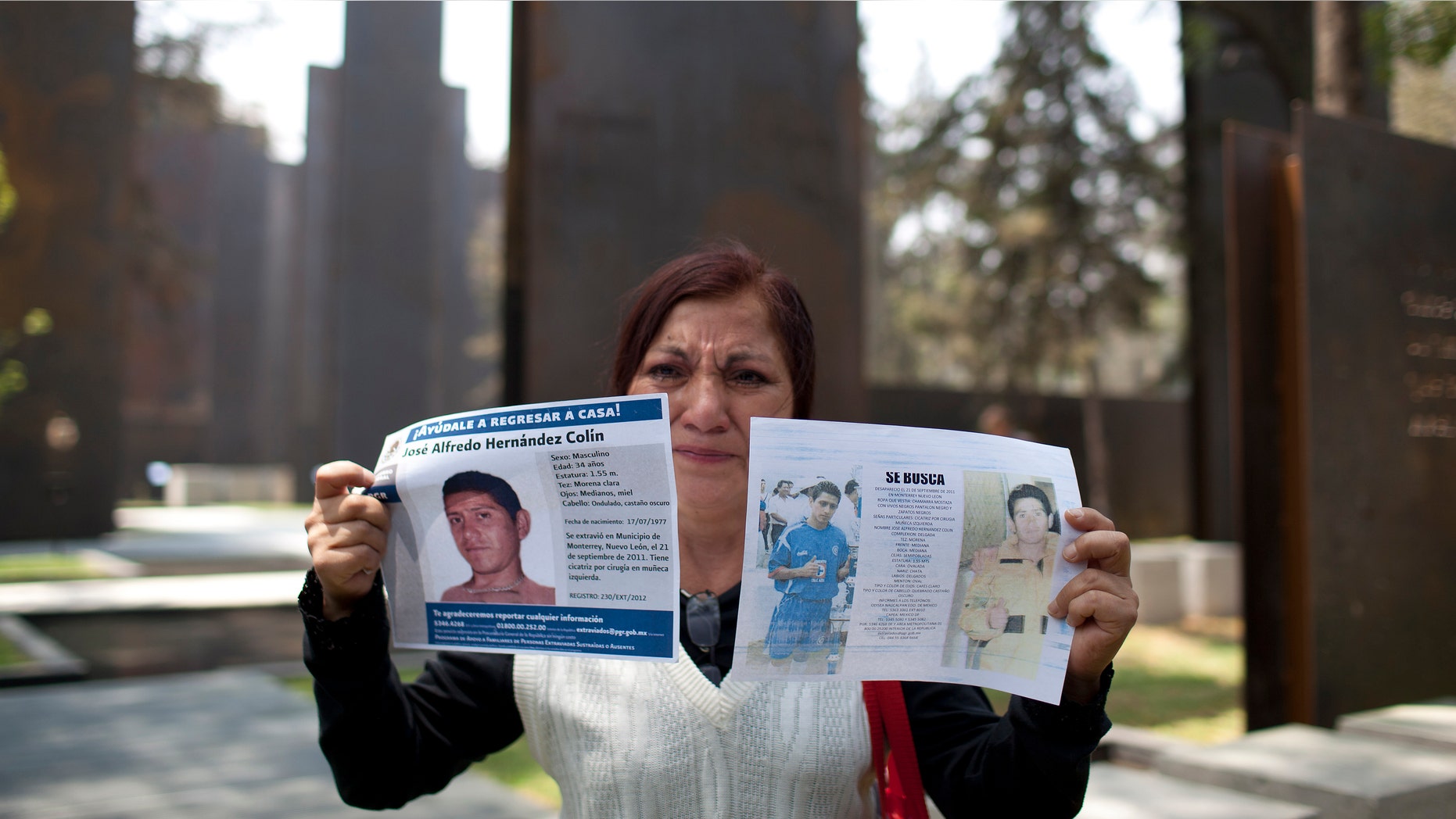 Yolanda Colin, shows leaflets with pictures of her nephew, Jose Alfredo Cilin, who went missing since 2011, as she stands by the new memorial in honor of victims of violence during its unveiling in Mexico City, Friday, April 5, 2013. The monument to the drug war dead consists of steel panels with nothing but few quotes from famous writers and thinkers. Activists who oppose the monument say the government needs to acknowledge each and every one of those killed. (AP Photo/Alexandre Meneghini)