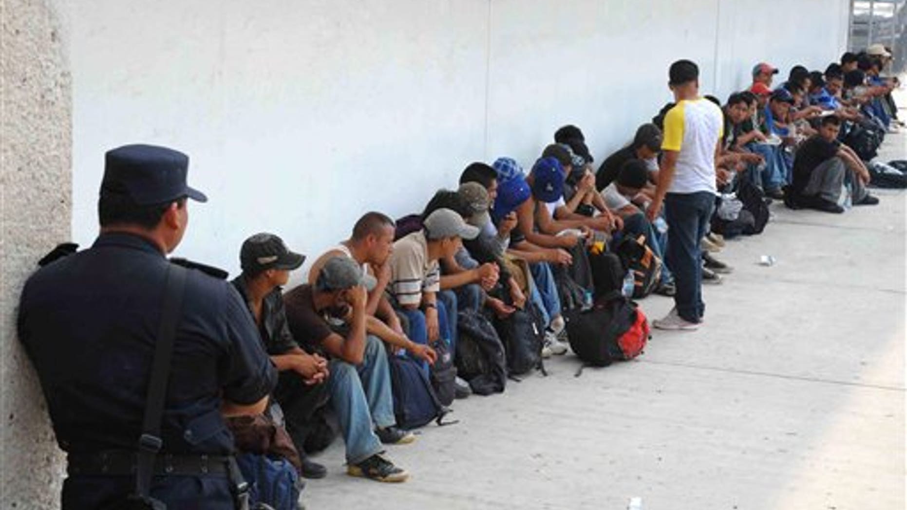 Migrants who were found in two trailer trucks bound for the United States, sit under the guard of a policeman in Tuxtla Gutierrez, Mexico, Tuesday May 17, 2011. Chiapas authorities say they rescued 513 migrants: 410 of the migrants were from Guatemala, 47 from El Salvador, 32 from Ecuador, 12 from India, six from Nepal, three from China and one each from Japan, the Dominican Republic and Honduras. (AP Photo/Alejandro Estrada)