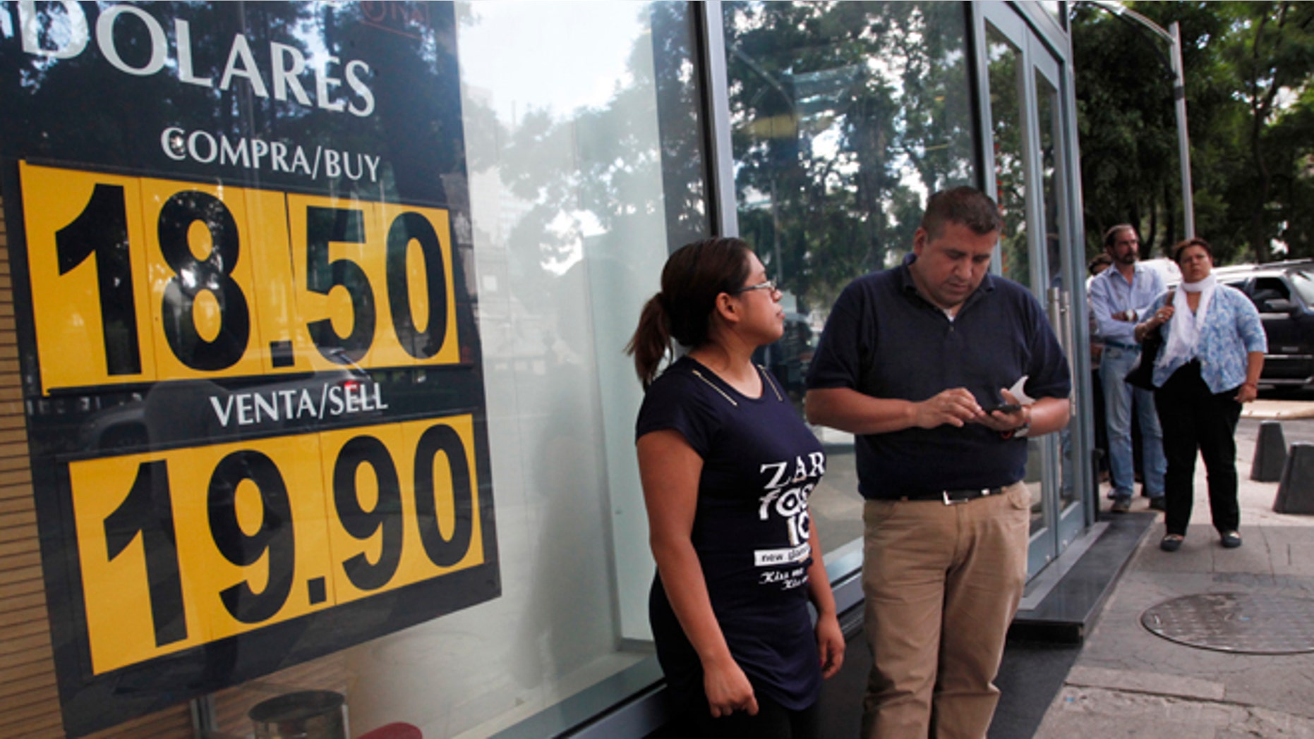 People stand outside an exchange house advertising the sale of U.S. dollars at the rate of 19.90 Mexican pesos per dollar in Mexico City, Monday, Sept. 19, 2016. The Mexican currency reached the psychological barrier of 20 pesos per dollar, and analysts and commentators cited the role of the U.S. presidential campaign. (Photo AP Photo / Marco Ugarte)