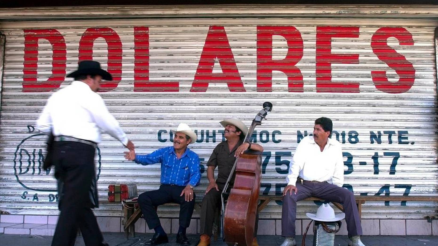 FILE - In this June 25, 2002 file photo, Northern Mexican musicians who play "Norteno" music greet each other as they wait for clients under a sign that reads "dollars" in Spanish in Monterrey, Mexico. Mexico's central bank says remittances sent home by Mexicans living abroad rebounded in 2014 after falling the previous year. Money sent home by Mexicans are one of the country's main sources of foreign income, along with oil exports. (AP Photo/Gregory Bull, File)