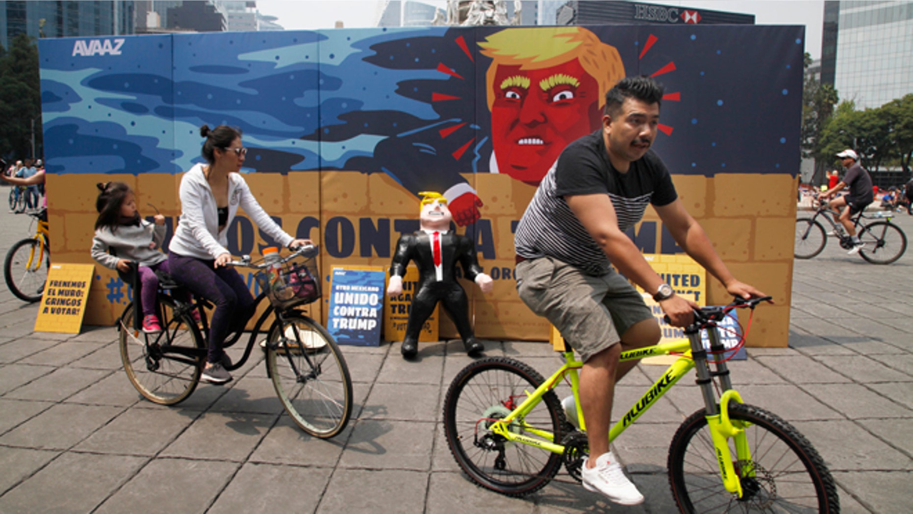 In this Sunday, Sept. 25, 2016 photo, a family of three ride their bicycles past a piñata depicting U.S. Republican presidential nominee Donald Trump propped against a cardboard mural wall with a message in Spanish that reads; "United against Trump" at the Angel of Independence monument in Mexico City. The head of Mexicoâs central bank told the Radio Formula network Friday, Sept. 30, 2016, that a Trump presidency âwould be a hurricane and a particularly intense one if he fulfills what he has been saying in his campaign.â (AP Photo/Marco Ugarte)