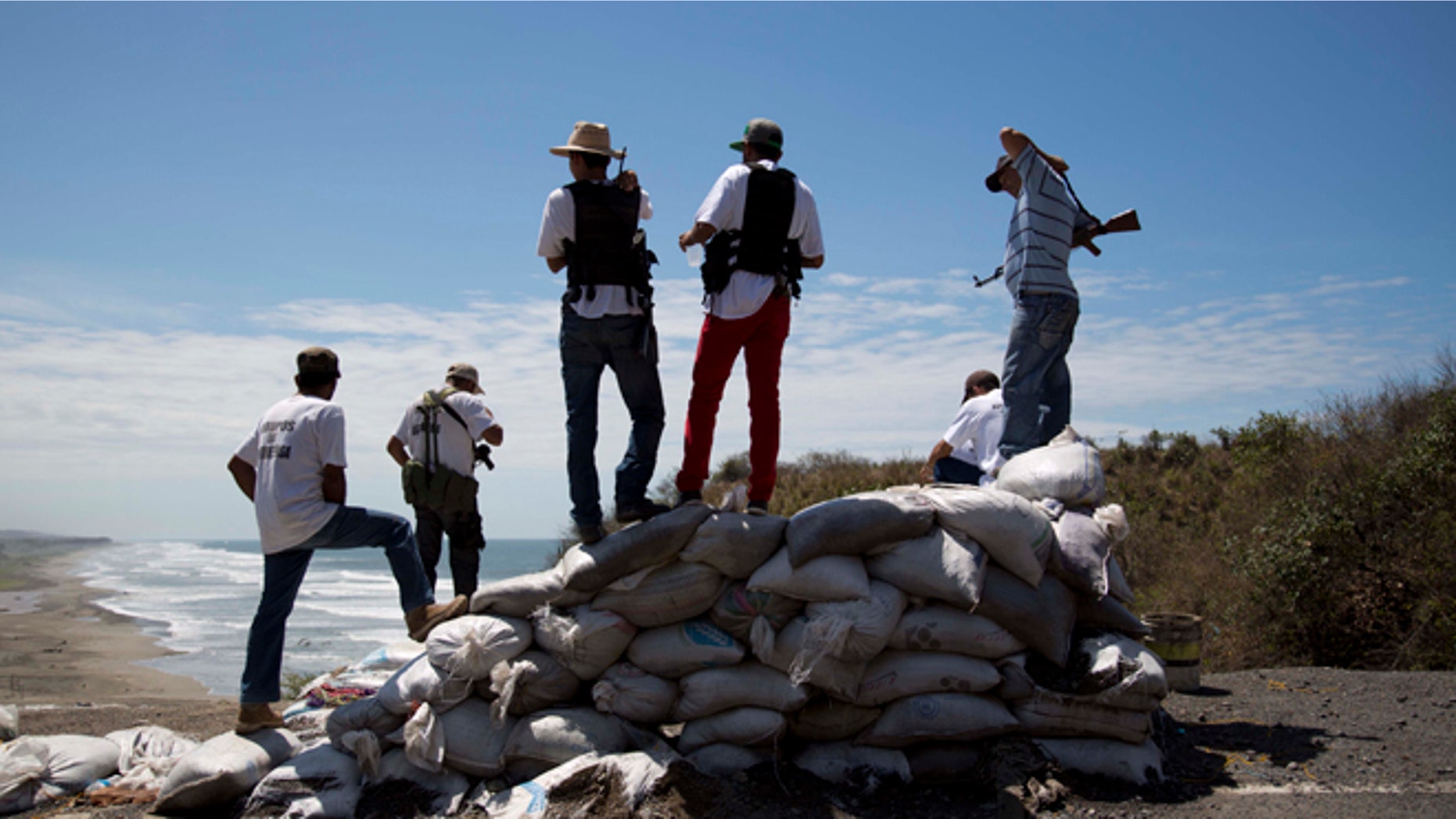 Armed men belonging to the Self-Defense Council of Michoacan (CAM) look out toward the sea as they guard a checkpoint set up by the self-defense group in Chuquiapan on the outskirts of the seaport of Lazaro Cardenas in western Mexico, Friday, May 9, 2014. Mexicos government plans on Saturday to begin demobilizing the vigilante movement that largely expelled the Knights Templar cartel when state and local authorities couldnt. But tension remained on Friday in the coastal part of the state outside the port of Lazaro Cardenas, where some self-defense groups plan to continue as they are, defending their territory without registering their arms. (AP Photo/Eduardo Verdugo)