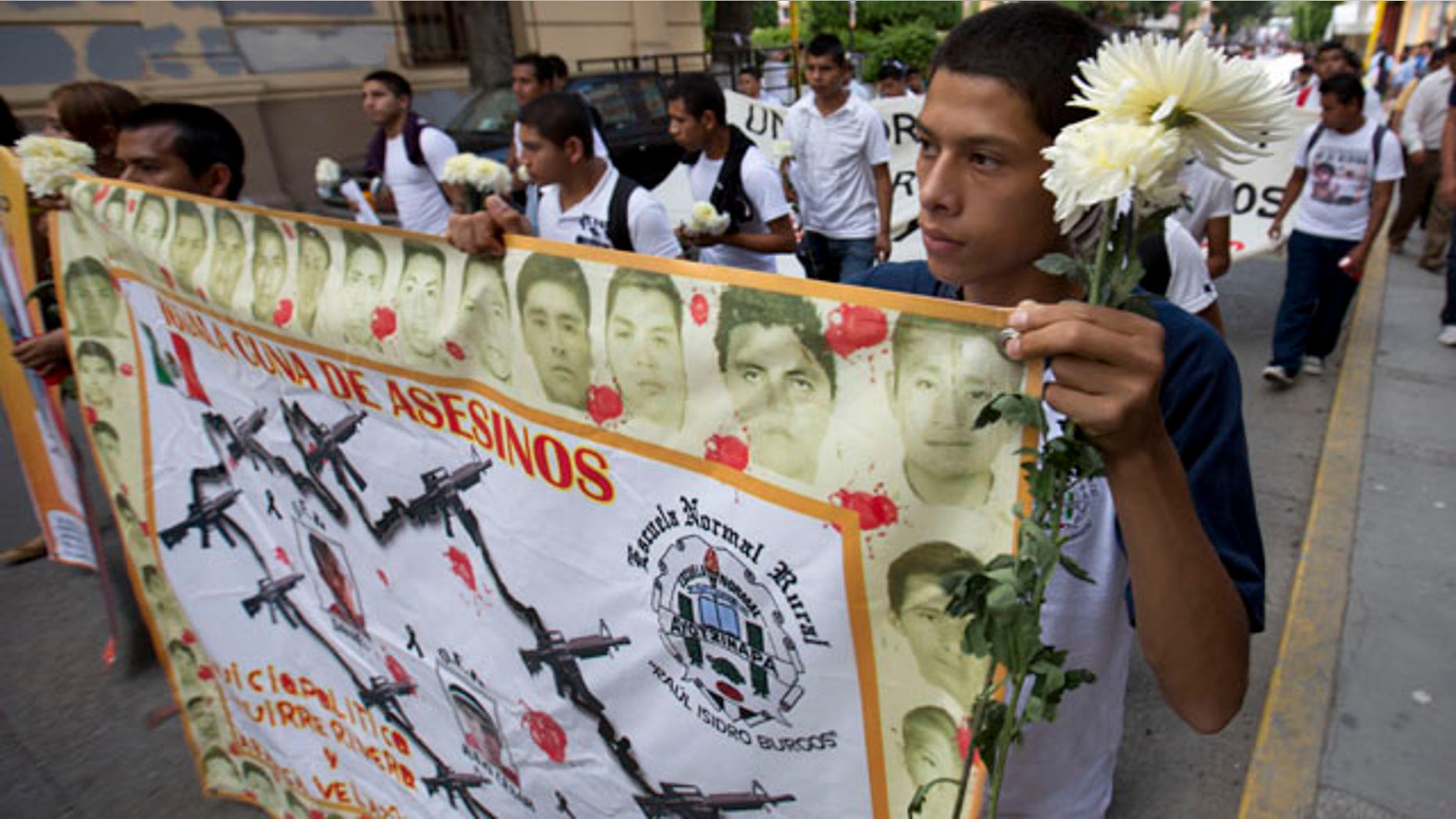 October 14, 2014: Students hold a banner with the faces of the missing that reads in Spanish 'cradle of murders' during a march with flowers and candles to protest the disappearance of 43 students from the Isidro Burgos rural teachers college in Chilpancingo, Mexico. (AP Photo/Eduardo Verdugo)