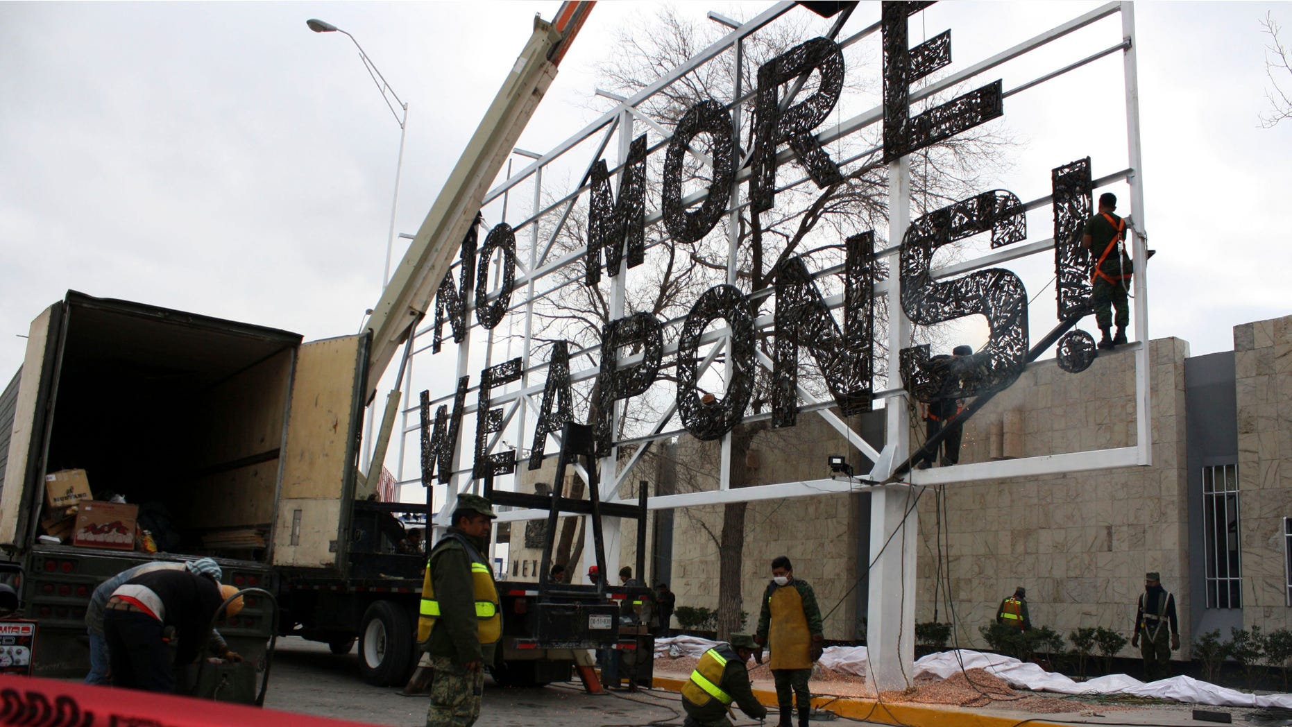 FILE - In this Feb. 17, 2012 file photo, soldiers put the final touches on a giant "No More Weapons" billboard made with crushed firearms placed near the U.S. border in Ciudad Juarez, Mexico. The once-embattled Mexican border city has taken down the billboard, one of the most visible reminders of its violence-laden recent past. Mayor Enrique Serrano said Wednesday, June 17, 2015 that the city wants to project a more tourist-friendly image. (AP Photo/Raymundo Ruiz, File)