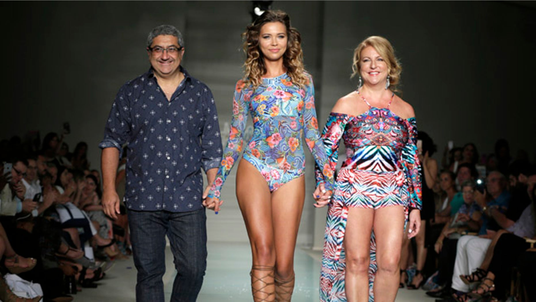 A model walks down the runway with designers Augusto Hanimian, left, and Lourdes "Luli" Hanimian during the Luli Fama swimwear show, Saturday, July 16, 2016, in Miami Beach, Fla. (AP Photo/Lynne Sladky)