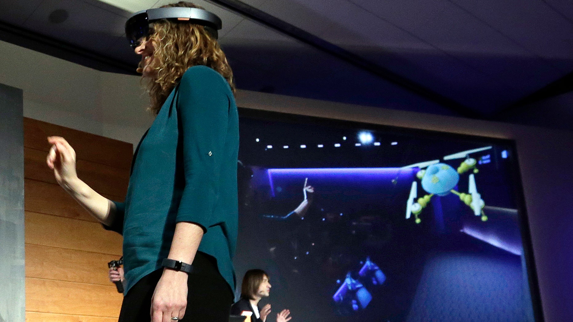 In this photo taken Wednesday, Jan. 21, 2015, Microsoft's Lorraine Bardeen demonstrates a hologram device as what she "sees" is projected on a screen behind during an event at the company's headquarters in Redmond, Wash.