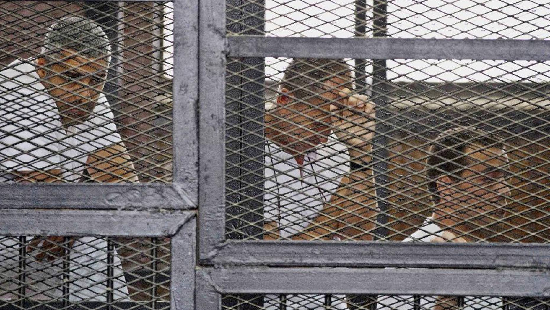 FILE - In this Thursday, May 15, 2014 file photo, from left, Mohammed Fahmy, Canadian-Egyptian acting bureau chief of Al-Jazeera, Australian correspondent Peter Greste, and Egyptian producer Baher Mohamed appear in a defendant's cage along with several other defendants during their trial on terror charges at a courtroom in Cairo. Egypt’s state news agency says the trial of three Al-Jazeera English journalists and 17 others has adjourned until next week when the judge will deliver the verdict, five months after the trial opened. Fahmy, Greste and Baher have been in detention since December 29. (AP Photo/Hamada Elrasam, File)