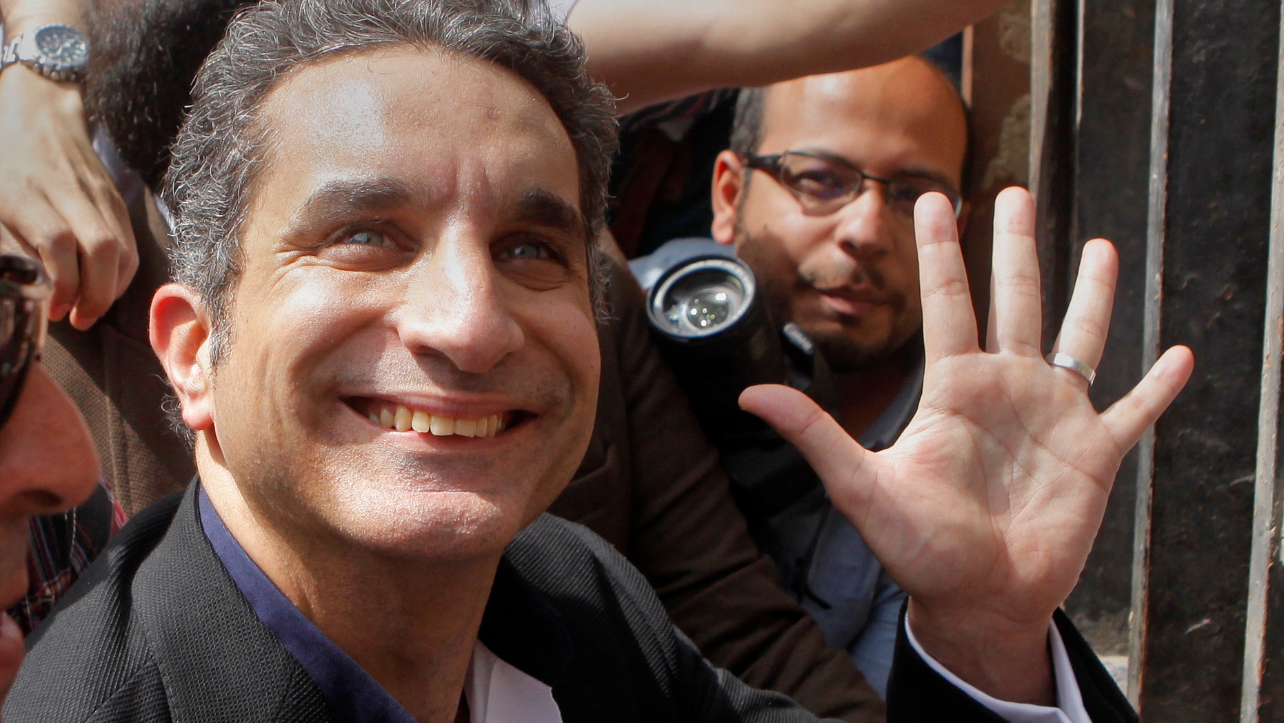 Popular Egyptian television satirist Bassem Youssef, who has come to be known as Egypt's Jon Stewart, waves to is supporters as he enters Egypt's state prosecutors office to face accusations of insulting Islam and the country's Islamist leader in Cairo, Egypt, Sunday, March 31, 2013. Government opponents said the warrant against such a high profile figure, known for lampooning President Mohammed Morsi and the new Islamist political class, was an escalation in a campaign to intimidate critics. (AP Photo/Amr Nabil)
