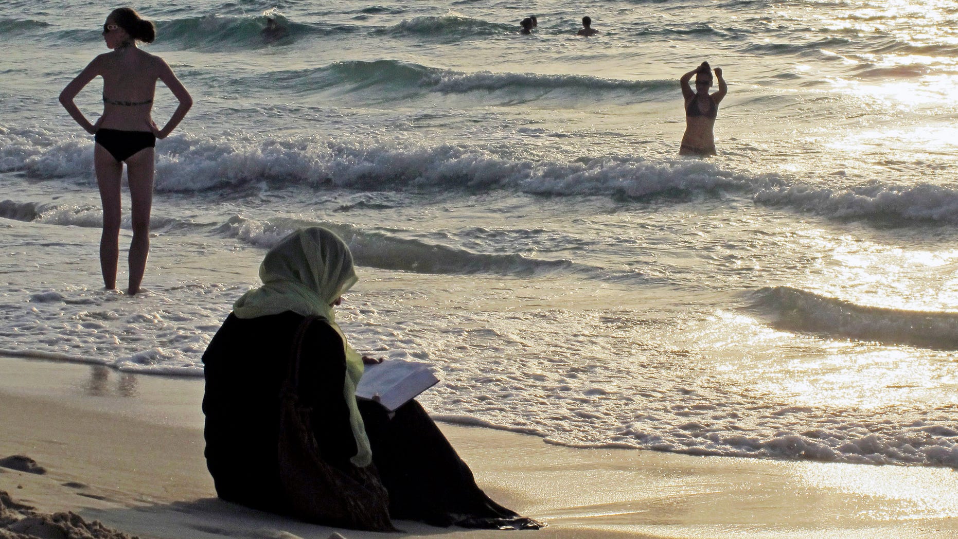 Sept. 6, 2012 - FILE photo of a woman reading the Koran on a beach as people in bikinis sunbathe and swim at sunset in Dubai, United Arab Emirates.