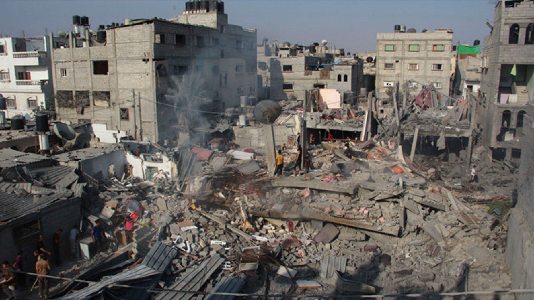 FILE - In this Saturday, Aug. 2, 2014 file photo, Palestinians stand on the rubble of houses destroyed in an Israeli strike in Rafah, southern Gaza Strip. (AP Photo/Hatem Ali, File)