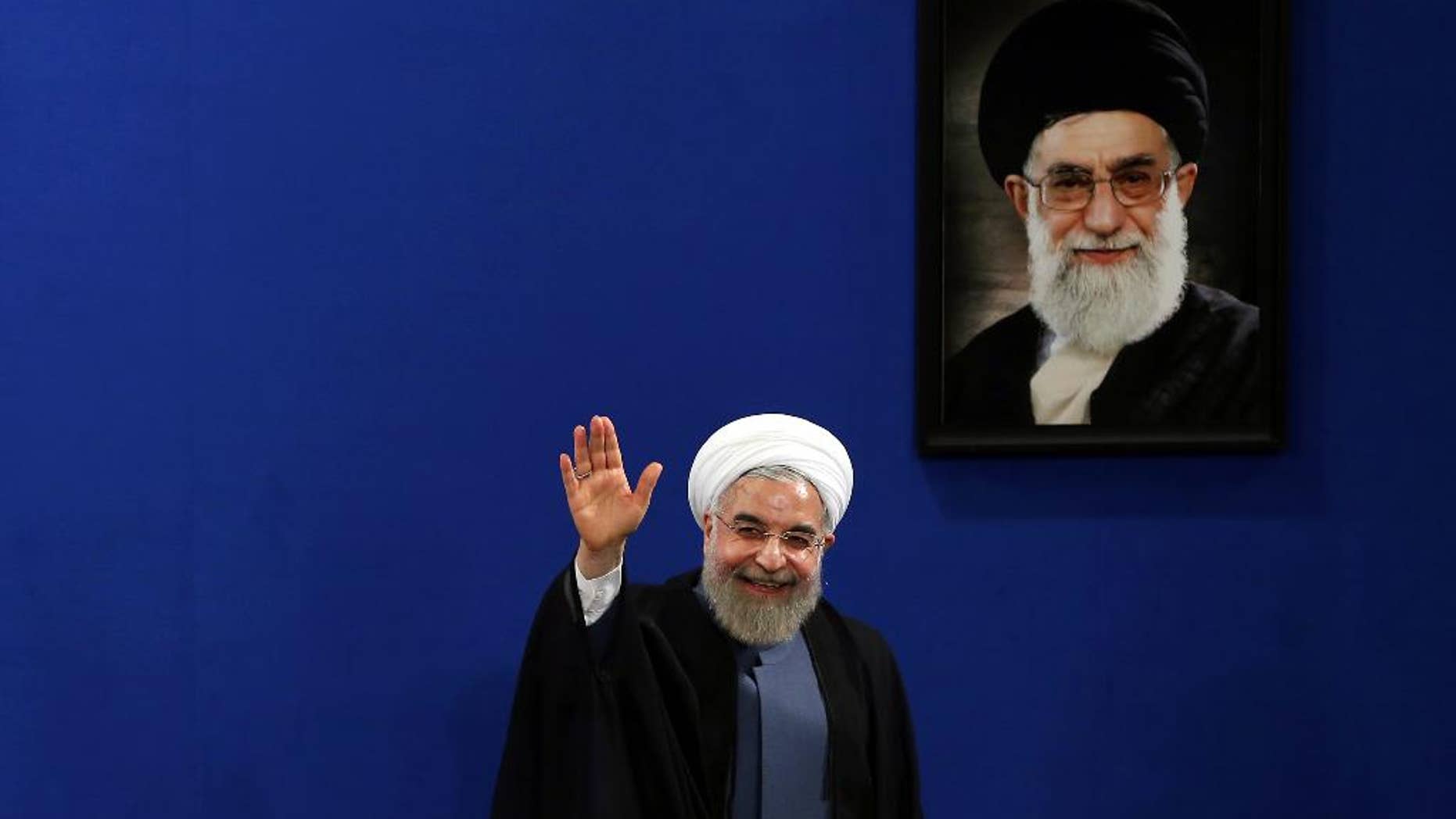 June 13, 2015: Iran's President Hassan Rouhani waves to reporters at the conclusion of his press conference on the second anniversary of his election, in Tehran, Iran. Rouhani said a final nuclear deal is "within reach" as Iran and world powers face a June 30 deadline for an agreement. A picture of the supreme leader Ayatollah Ali Khamenei hangs on the wall.