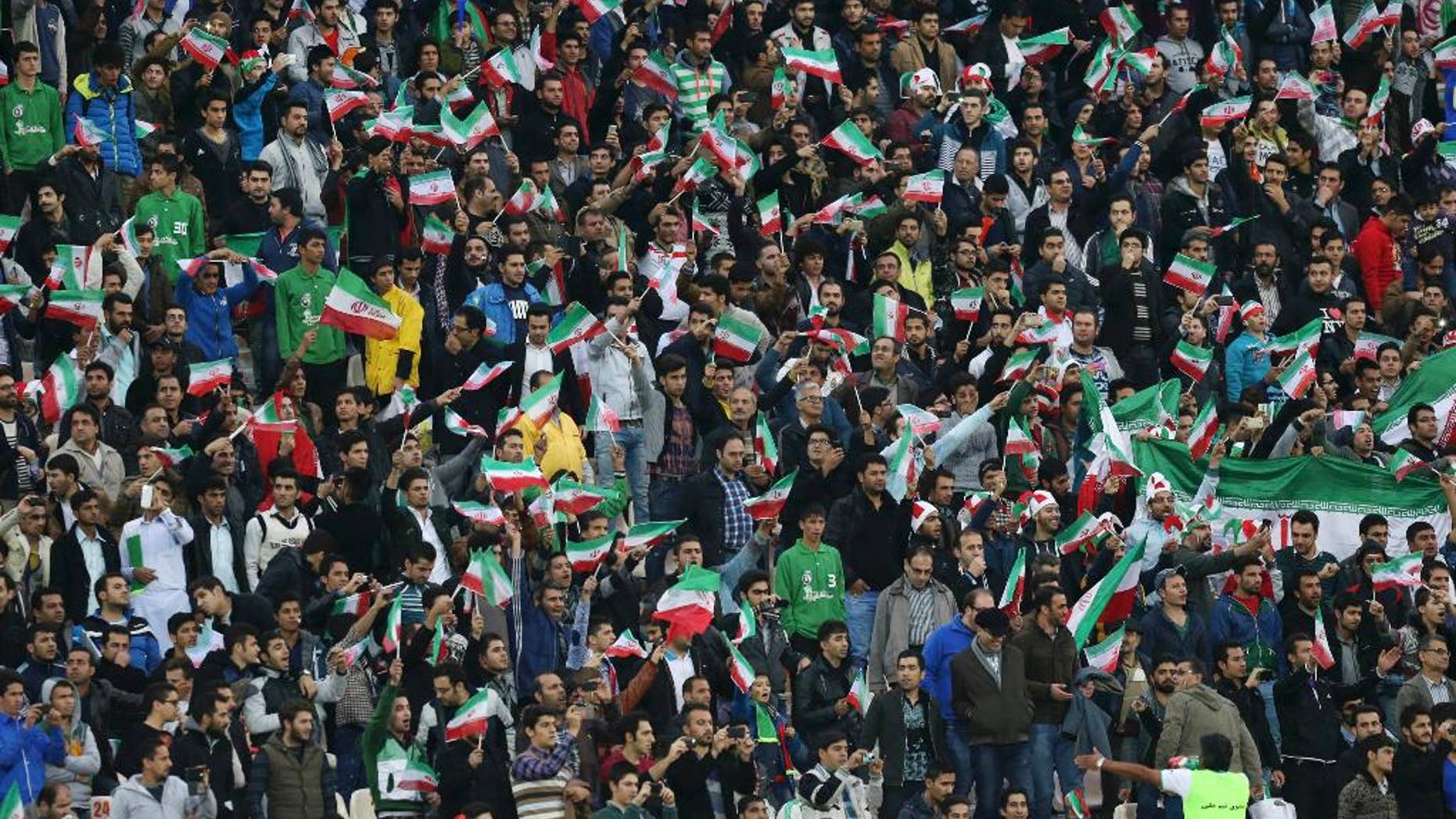 FILE - In this Nov. 18, 2014 file photo, Iranian soccer supporters wave their country's flag while following a friendly match between Iran and South Korea at the Azadi, (freedom) stadium in Tehran, Iran. Iranian authorities have partially lifted a ban on women attending men's sports matches, a senior sports official said Saturday, April 4, 2015. The announcement comes after FIFA President Sepp Blatter urged Iran last month to end the "intolerable" ban on women watching football in stadiums. (AP Photo/Vahid Salemi, File)