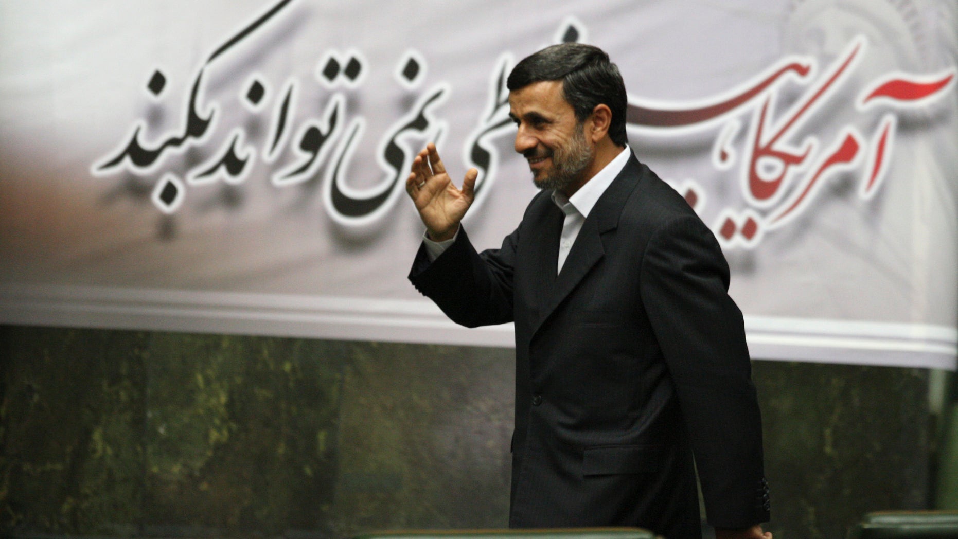 Nov. 2, 2011: Iranian President Mahmoud Ahmadinejad, waves, as he arrives to attend an open session of parliament for impeachment of his Economy Minister, Shamsoddin Hosseini, unseen, as a banner hangs behind him with a quotation of late revolutionary founder Ayatollah Khomeini, which says "US can not do anything", in Tehran, Iran.