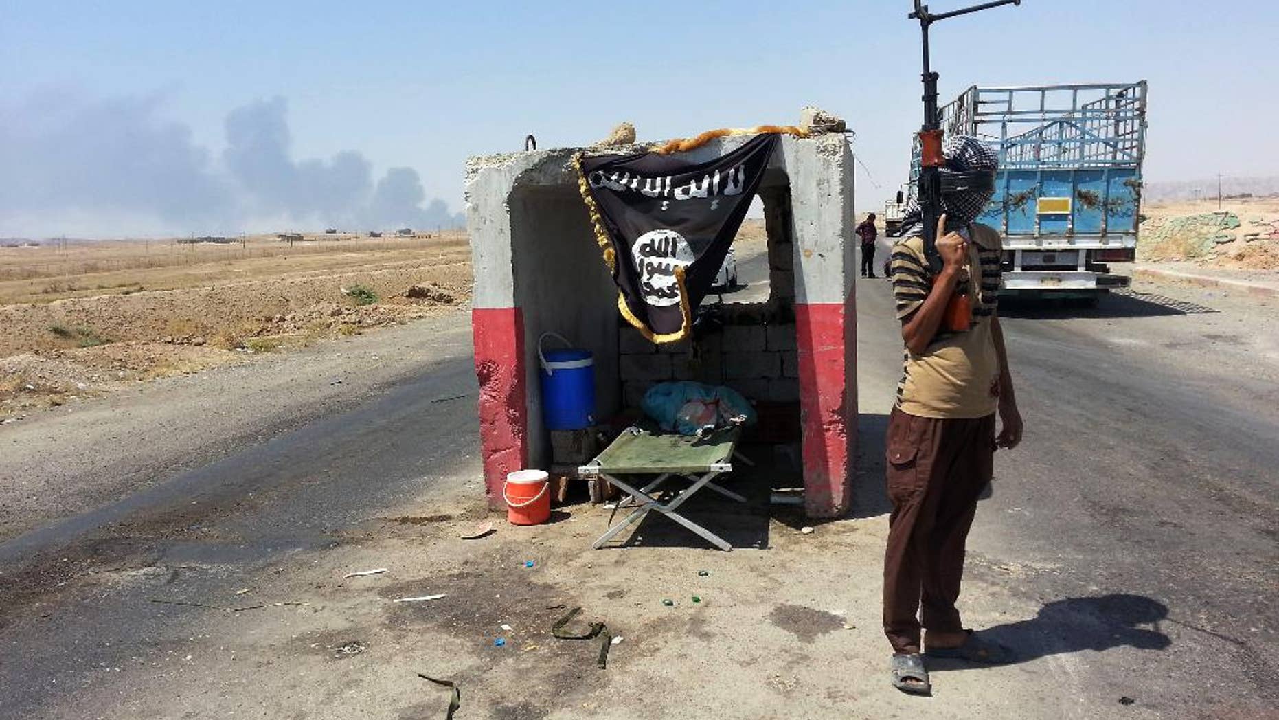 FILE - In this file photo taken Thursday, June 19, 2014, an al-Qaida-inspired militant stands guard at a checkpoint captured from the Iraqi Army outside Beiji refinery, some 250 kilometers (155 miles) north of Baghdad, Iraq. As Islamic militants rampaged across northern Iraq in June, seizing vast swaths of territory and driving hundreds of thousands of people from their homes, the Shiite Turkmens living in the hardscrabble town of Amirli decided to stay and fight. (AP Photo, File)