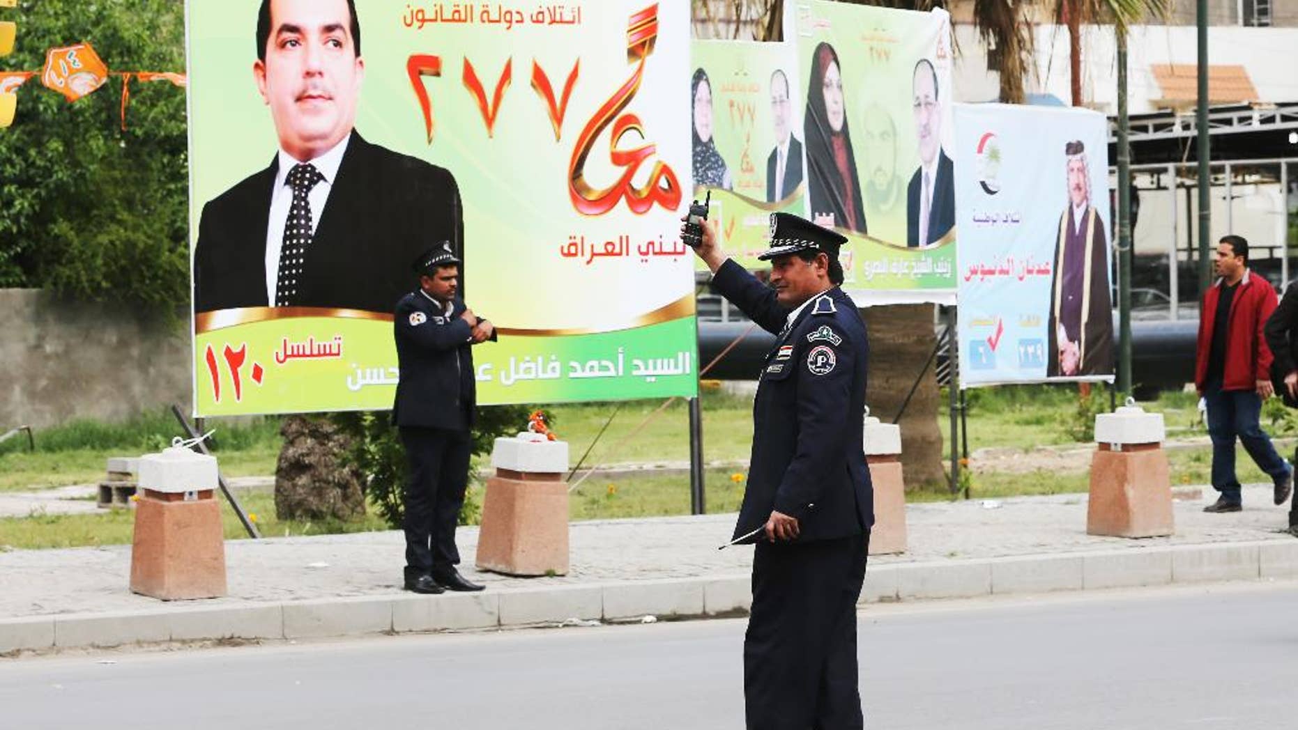 Iraqi traffic police officers control traffic in front of election campaign posters in Baghdad, Iraq,Tuesday April 1, 2014. The election campaign kicked off Tuesday with Iraqi towns and cities flooded with posters of the candidates for parliament seats on main streets and intersections. (AP Photo/Karim Kadim)