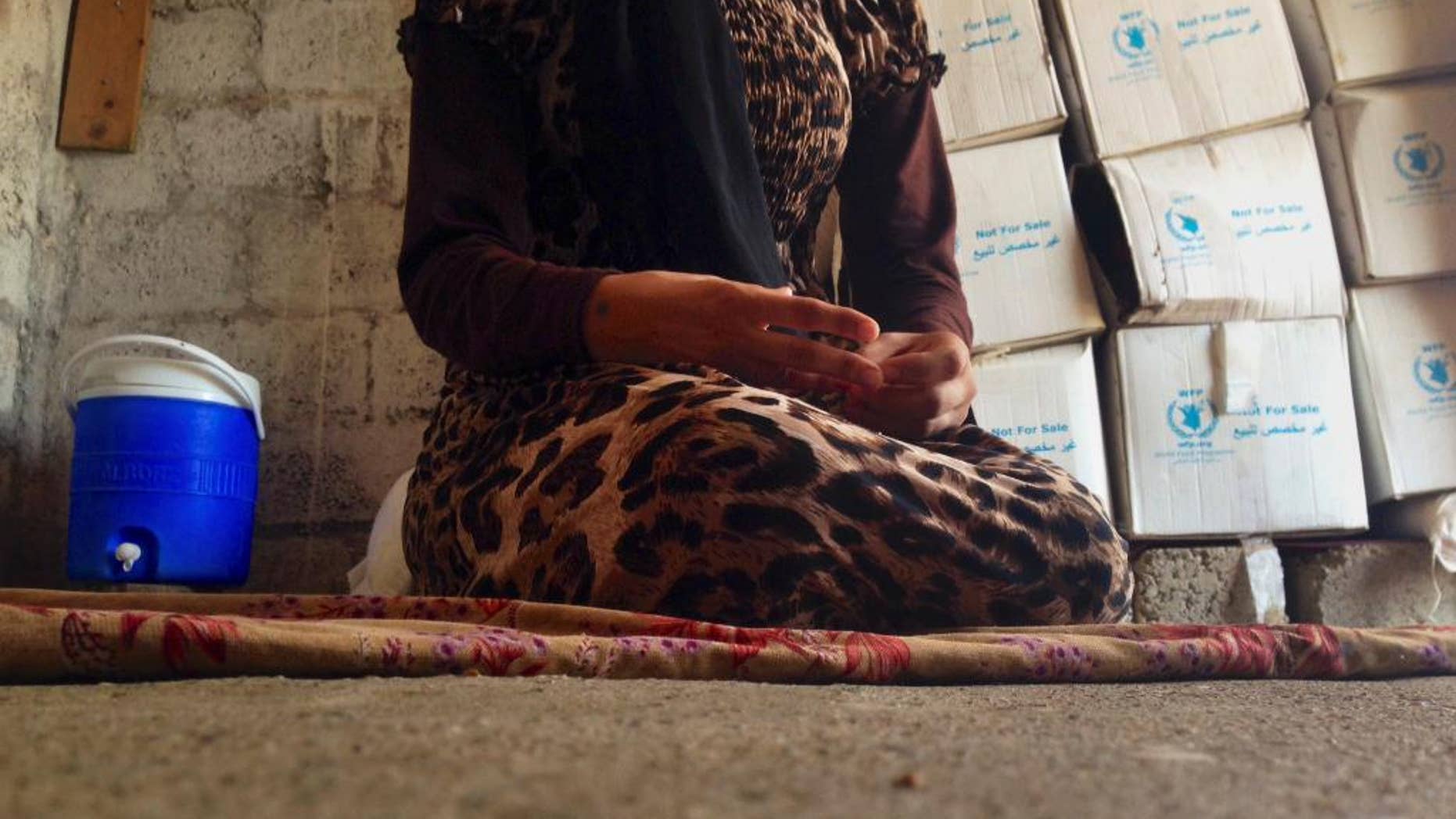 In this photo taken Wednesday, Oct. 8, 2014, a 15-year-old Yazidi girl captured by the Islamic State group and forcibly married to a militant in Syria sits on the floor of a one-room house she now shares with her family after escaping in early August, while speaking in an interview with The Associated Press in Maqluba, a hamlet near the Kurdish city of Dahuk, 260 miles (430 kilometers) northwest of Baghdad, Iraq. The girl was among hundreds of women and girls from the Yazidi religious minority captured by Islamic State fighters in early August when the militants overran their hometown of Sinjar in northwestern Iraq. Hundreds were killed in the attack, and tens of thousands fled for their lives, most to Kurdish-held parts of the north. (AP Photo/Dalton Bennett)