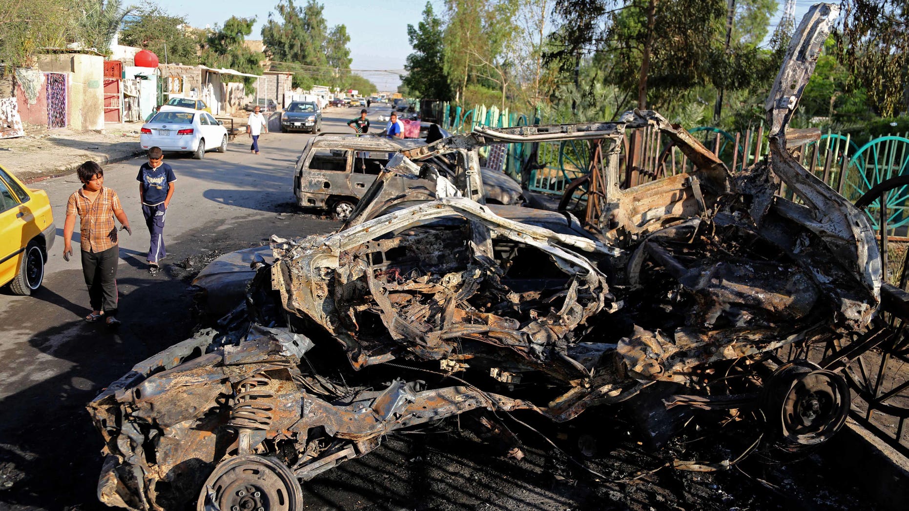 May 16, 2014 - Iraqi boys walk past destroyed vehicles the day after a car bomb attack near an outdoor market in Baghdad's Shiite neighborhood of Sadr City, Iraq. Bombings and shootings around Iraq's capital killed and wounded dozens of people Thursday, officials said.