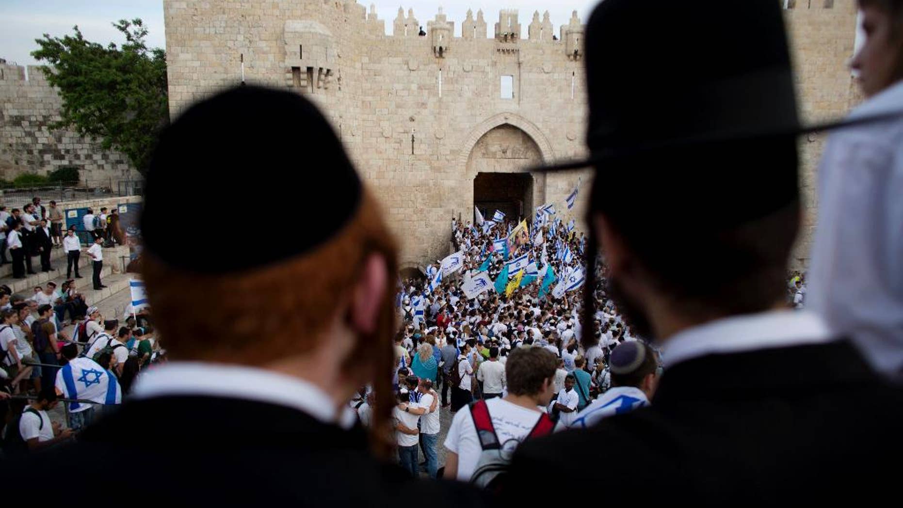 FILE - In this May 28, 2014, file photo, Ultra-Orthodox Jews watch people wave Israeli flags outside the Old City's Damascus Gate during Jerusalem Day celebrations in Jerusalem. A recent demonstration by ultra-Orthodox Jews against a new cinema opening its doors on the Sabbath was meant to be a show of strength in a long-running battle over the role of strict Jewish law in the cultural life of Jerusalem. But in many ways, it was also a sign of desperation after a series of gains by the city’s secular community in recent years. (AP Photo/Dusan Vranic, File)