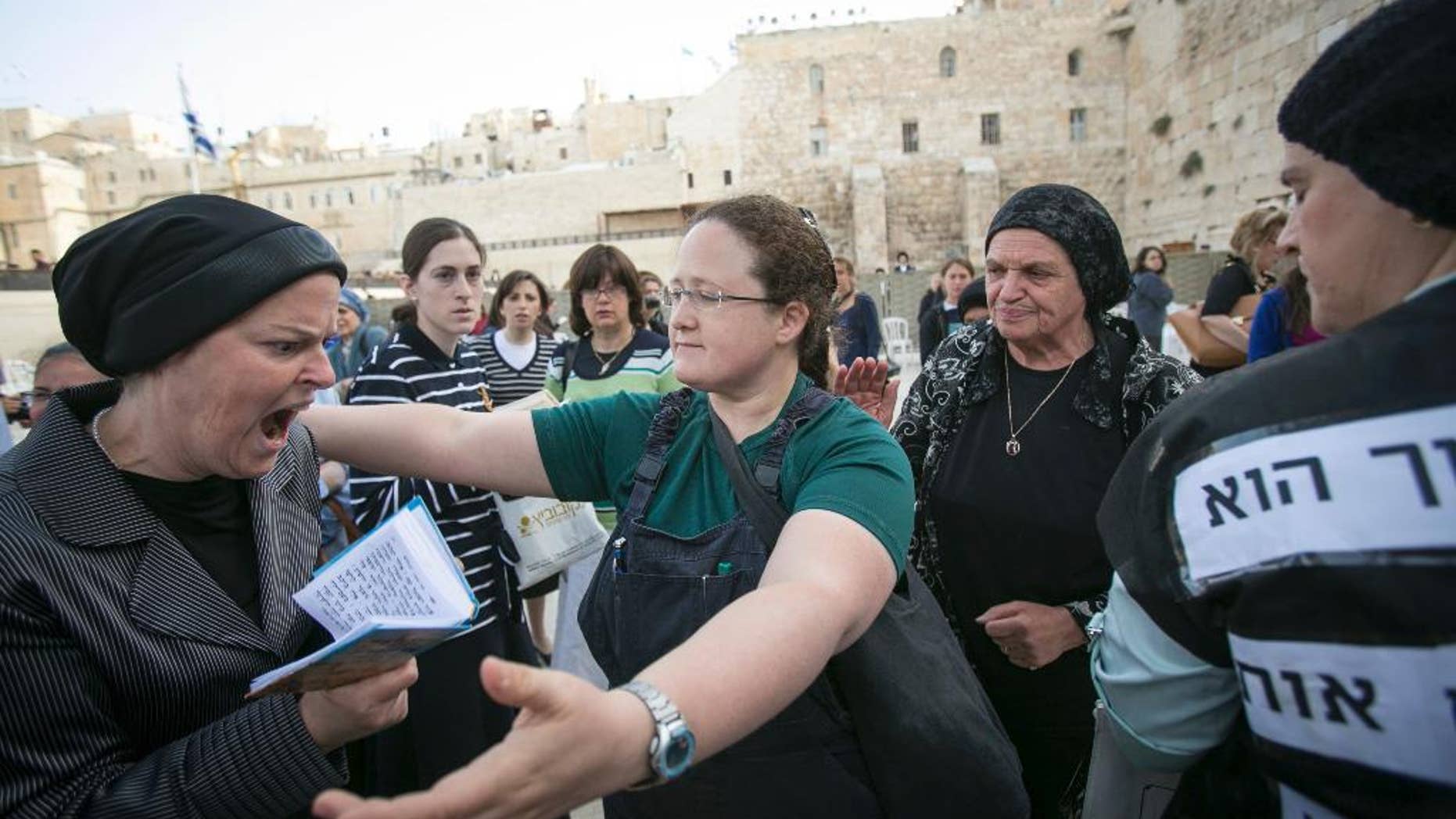 FILE - In this June 9, 2013 file photo, an Israeli member of the "Woman of the Wall" organization, right, tries to hug an ultra-Orthodox woman as they pray at the Western Wall, the holiest site where Jews can pray, in Jerusalem's old city. Israeli police say dozens of ultra-Orthodox Jews attacked buses bearing photos of women worshipping like men do. The advertisements on the buses were by Women of the Wall, a group that seeks to promote gender equality at Jerusalem's Western Wall, the holiest site where Jews can pray. The ads showed women and girls holding Torah scrolls, an act which many Orthodox Jews say is reserved for men. (AP Photo/Michal Fattal,File) ISRAEL OUT