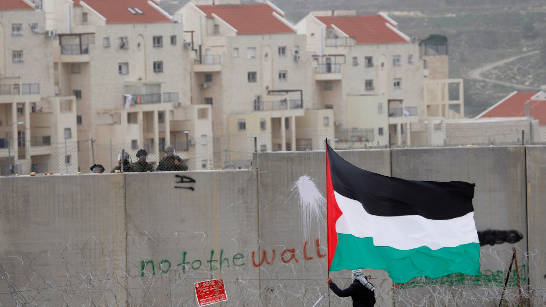 Feb. 17, 2012: In this file photo, the West Bank Jewish settlement of Modiin Illit is seen in the background while a protestor waves a Palestinian flag in front of Israeli troops during a protest against Israel's separation barrier in the West Bank village of Bilin.