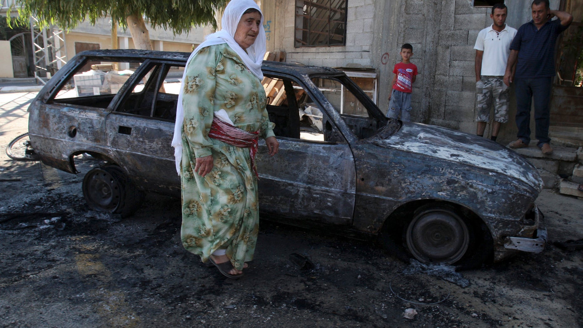 A Palestinian woman walks next to a burnt car in the village of Beit Furik, near the West Bank town of Nablus, Thursday, Sept. 15, 2011.
