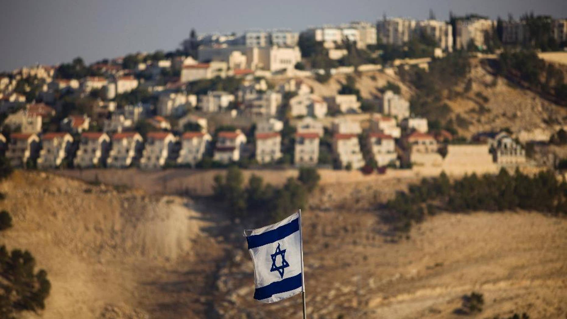FILE - In this Monday, Sept. 7, 2009 file photo, an Israeli flag is seen in front of the West Bank Jewish settlement of Maaleh Adumim on the outskirts of Jerusalem. The population of Jewish settlers in the occupied West Bank has surged during Prime Minister Benjamin Netanyahu's years in office, growing at more than twice the pace of the overall population, according to official figures obtained in December, 2014. (AP Photo/Bernat Armangue, File)