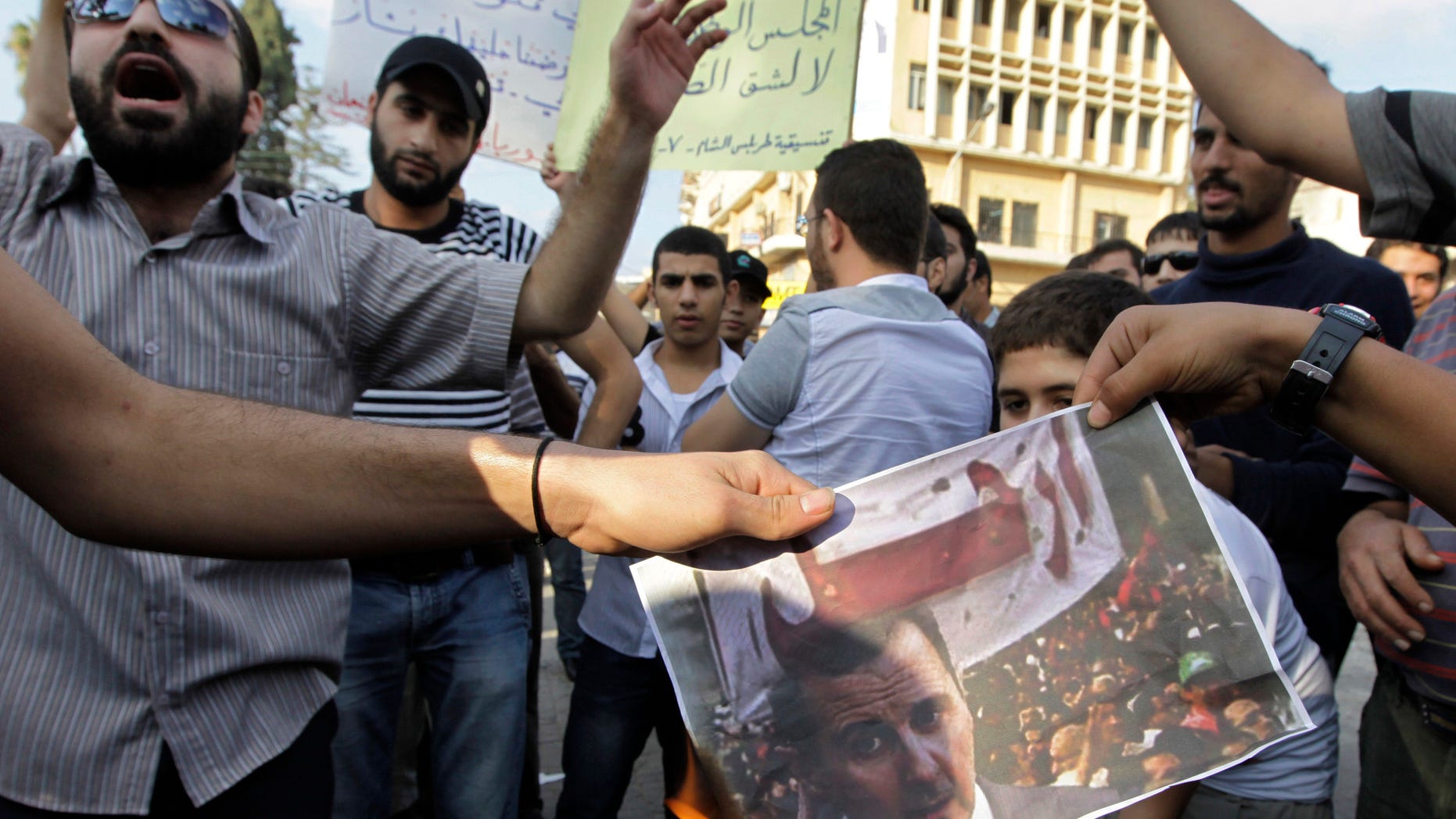 Anti-Syrian regime protesters burn a portrait of Syrian President Bashar Assad with Arabic words read: "Leave," as they protest after Friday prayers in a show of support for Syrians protesting against Syrian President Bashar Assad, in the northern city of Tripoli, Lebanon, on Friday Oct, 7, 2011.